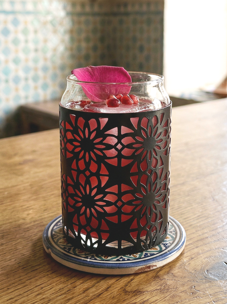 Moroccan inspired lattice cocktail glass serving a rose and pomegrante cocktail sitting on a bar top in a moroccan style cafe table