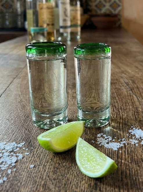 Hand blown green rimmed shot glass from mexico on a bar top in a mexican cantina