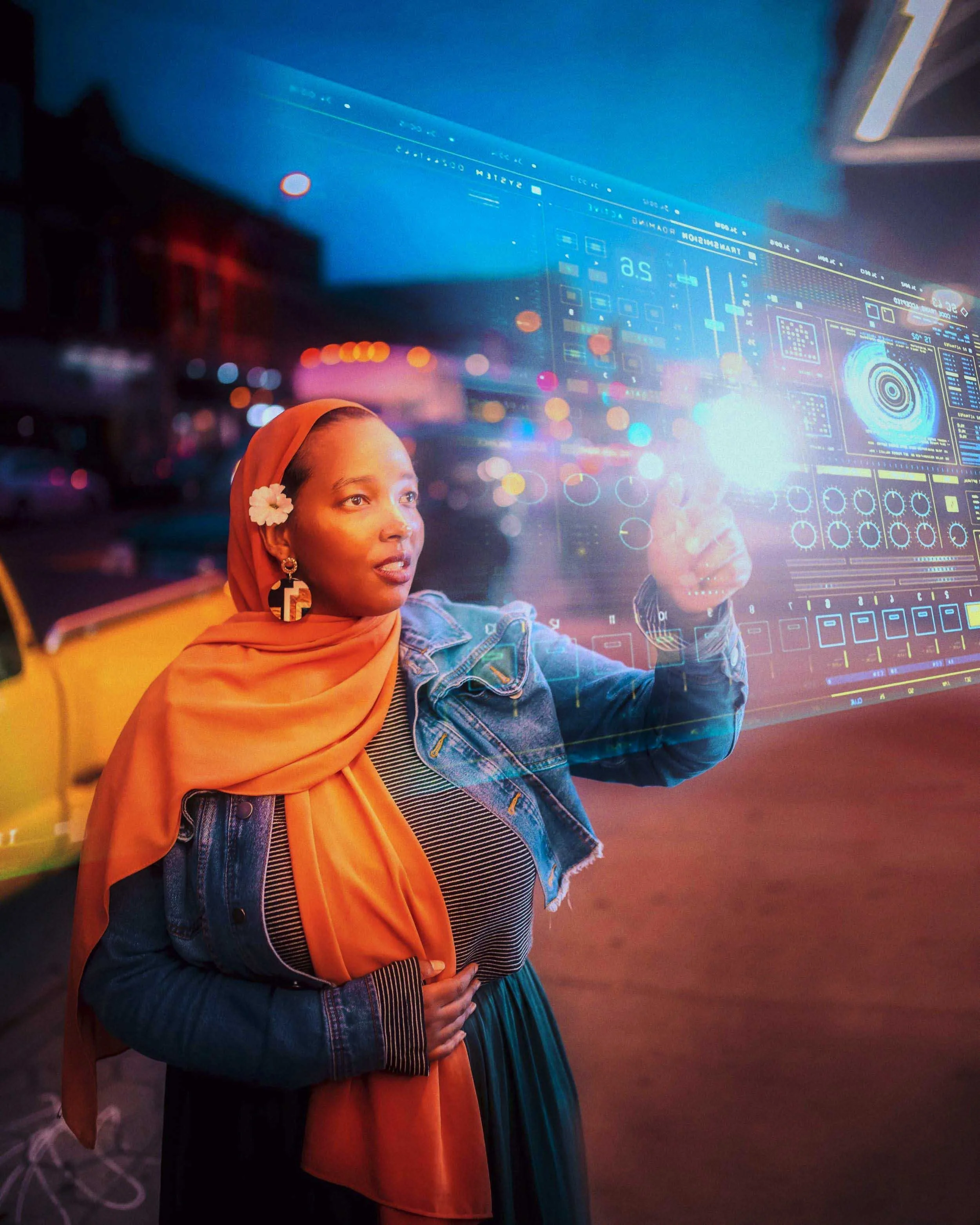 A woman in a denim jacket and orange hijab interacts with a large digital screen displaying a futuristic interface with charts and data, illuminated by a bright light, with a blurred cityscape background at dusk.