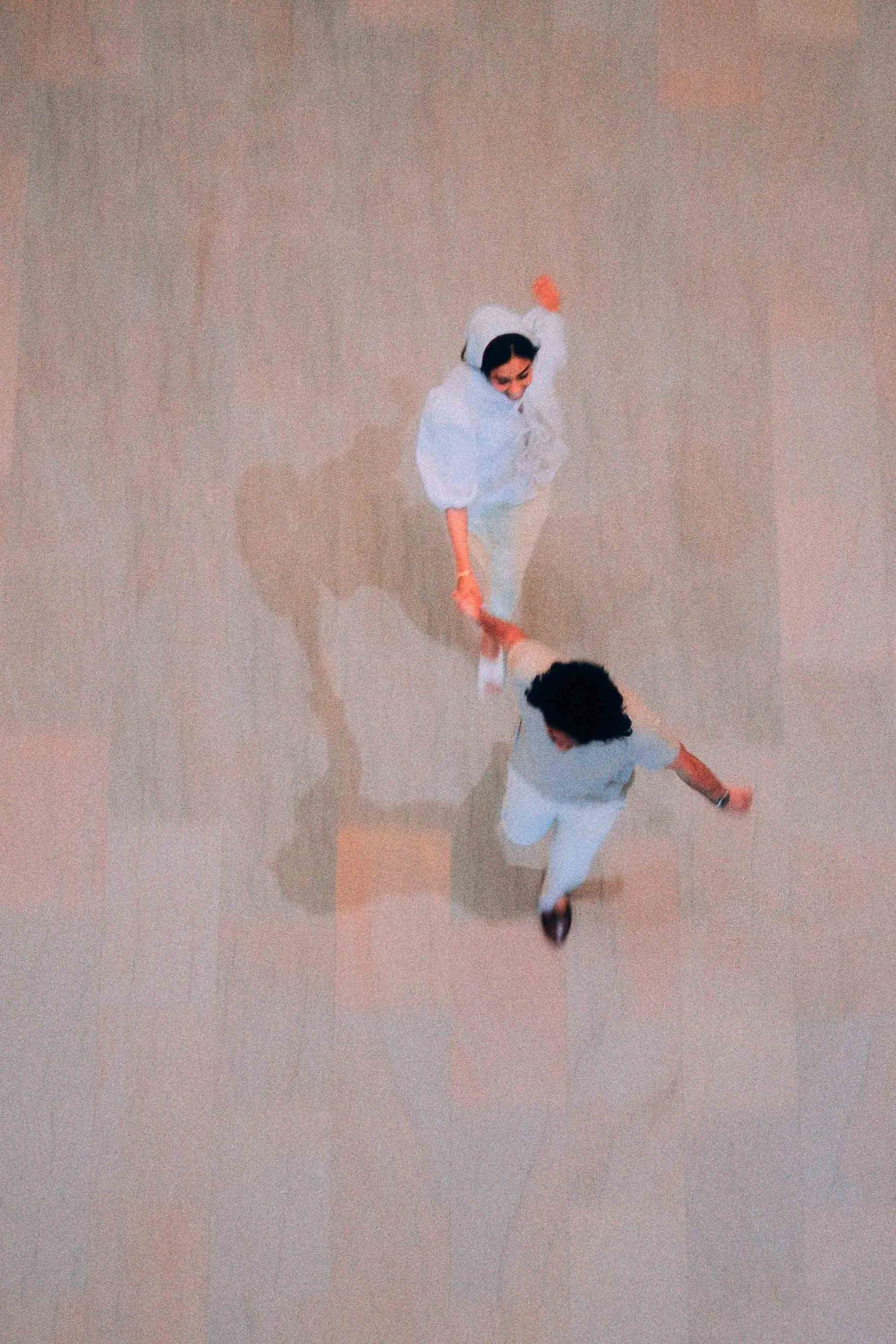 Two people dancing in formal attire, holding hands, on a shiny floor with their shadows visible.