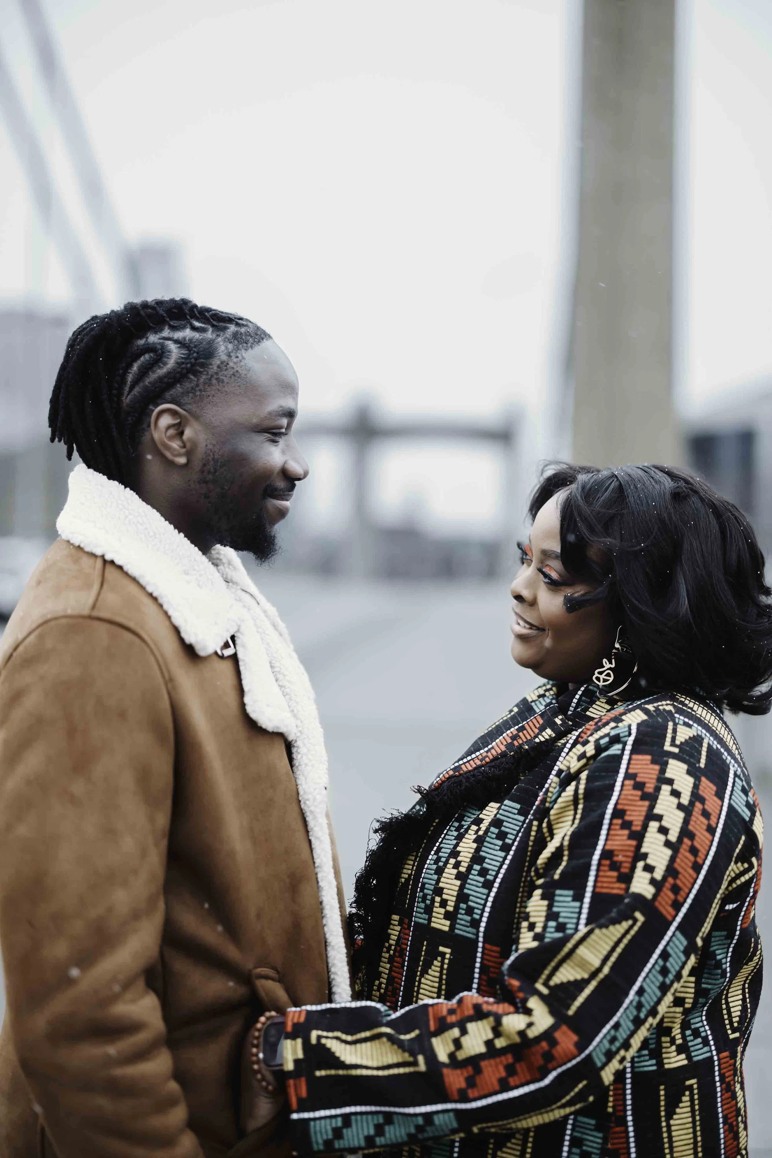 A man and woman standing face to face outdoors, smiling at each other.