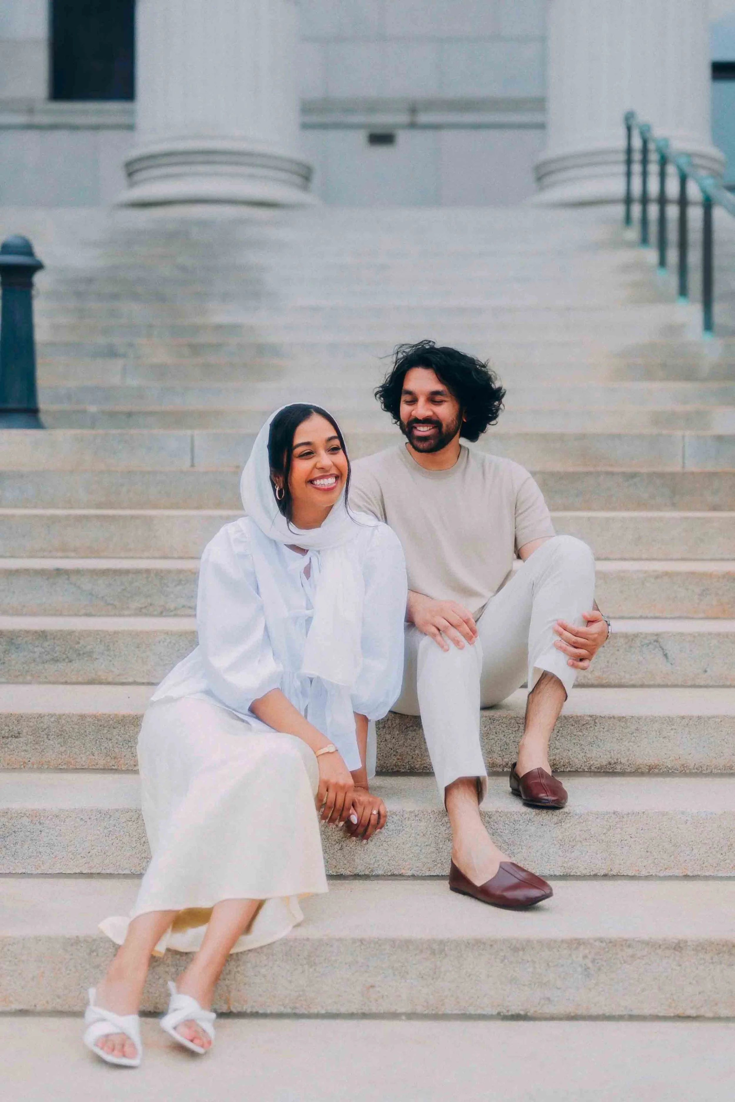 Two people sitting on steps, smiling, in front of a building with large columns.