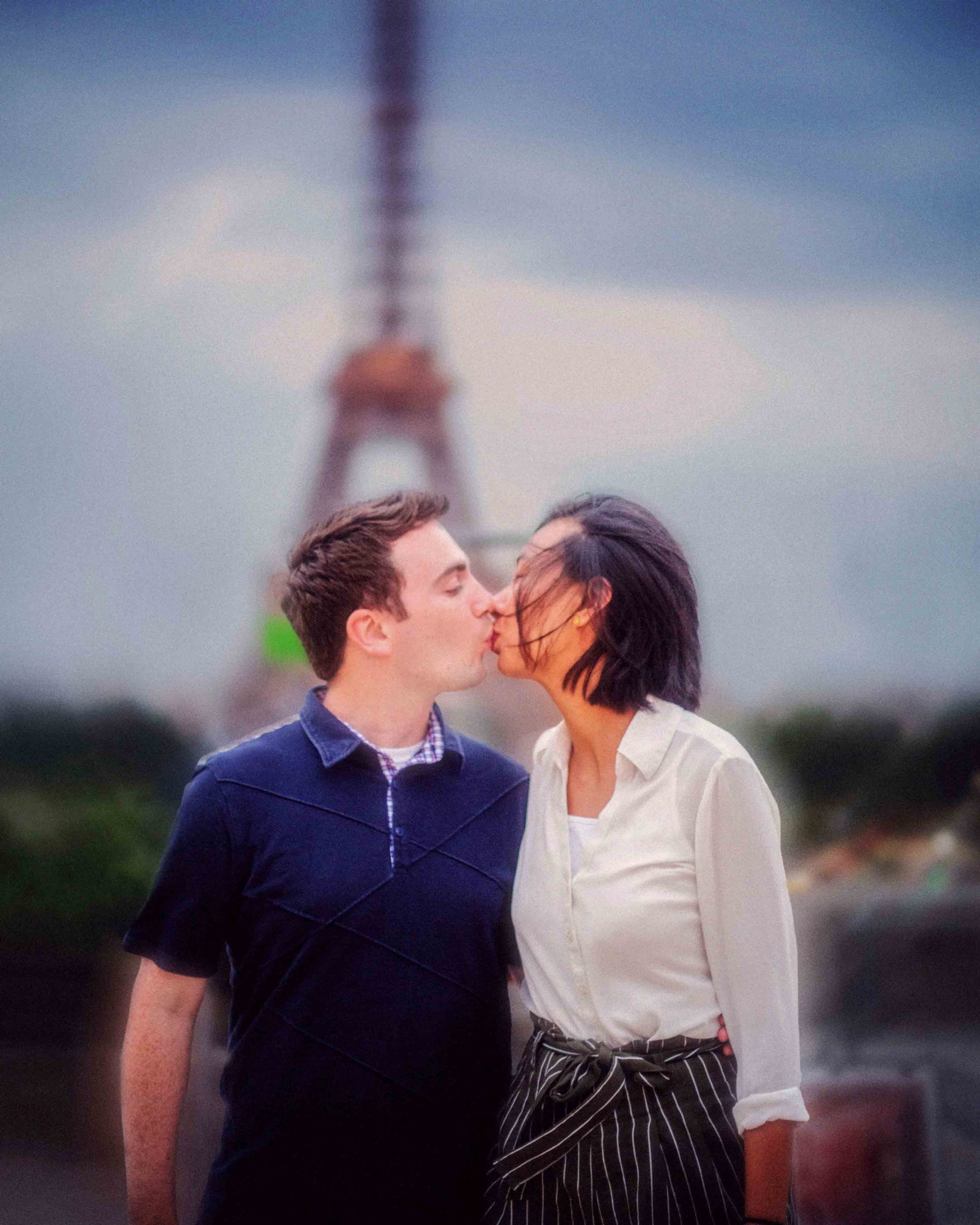 A couple is kissing in front of the Eiffel Tower in Paris, France during the evening.