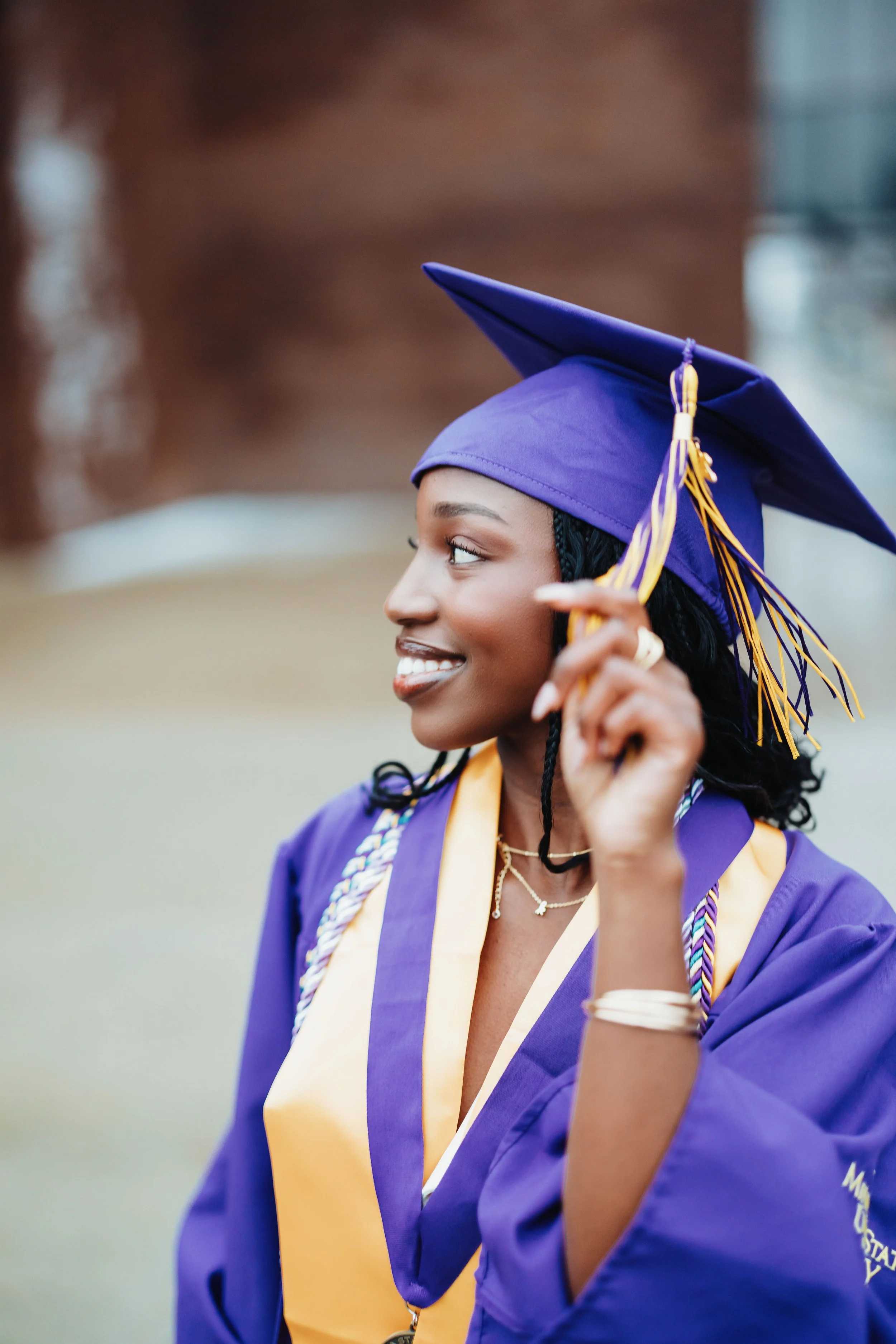 A young woman in a purple graduation cap and gown smiling and adjusting her cap.