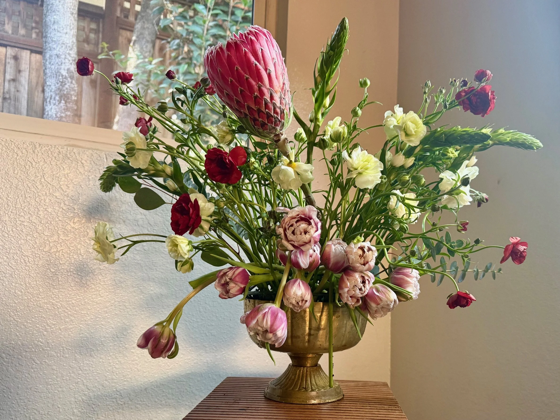 Centerpiece featuring pink protea, pink parrot tulips in a gold compote vase