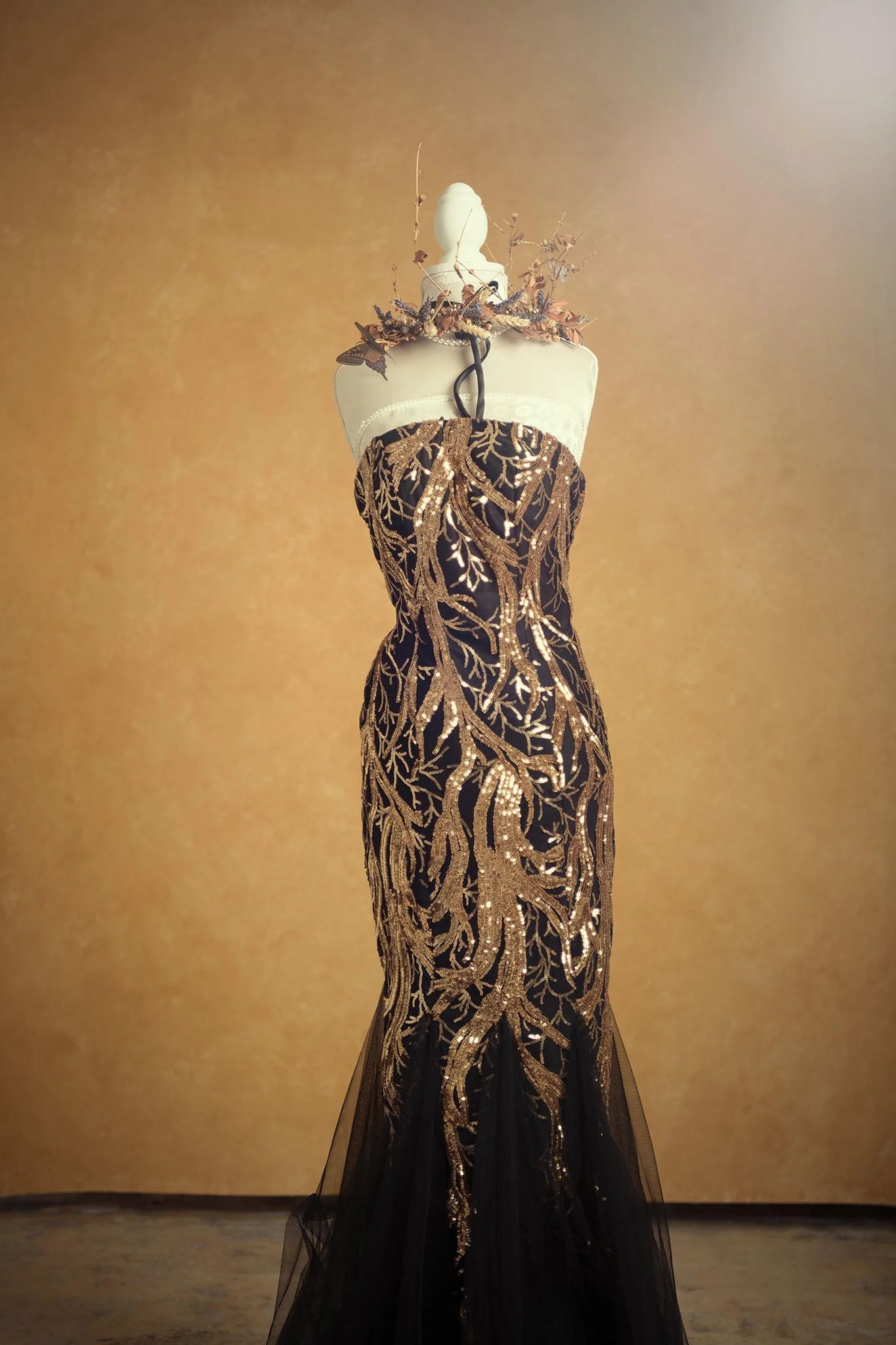 Elegant black evening gown with gold embroidery displayed on a mannequin against a beige background.