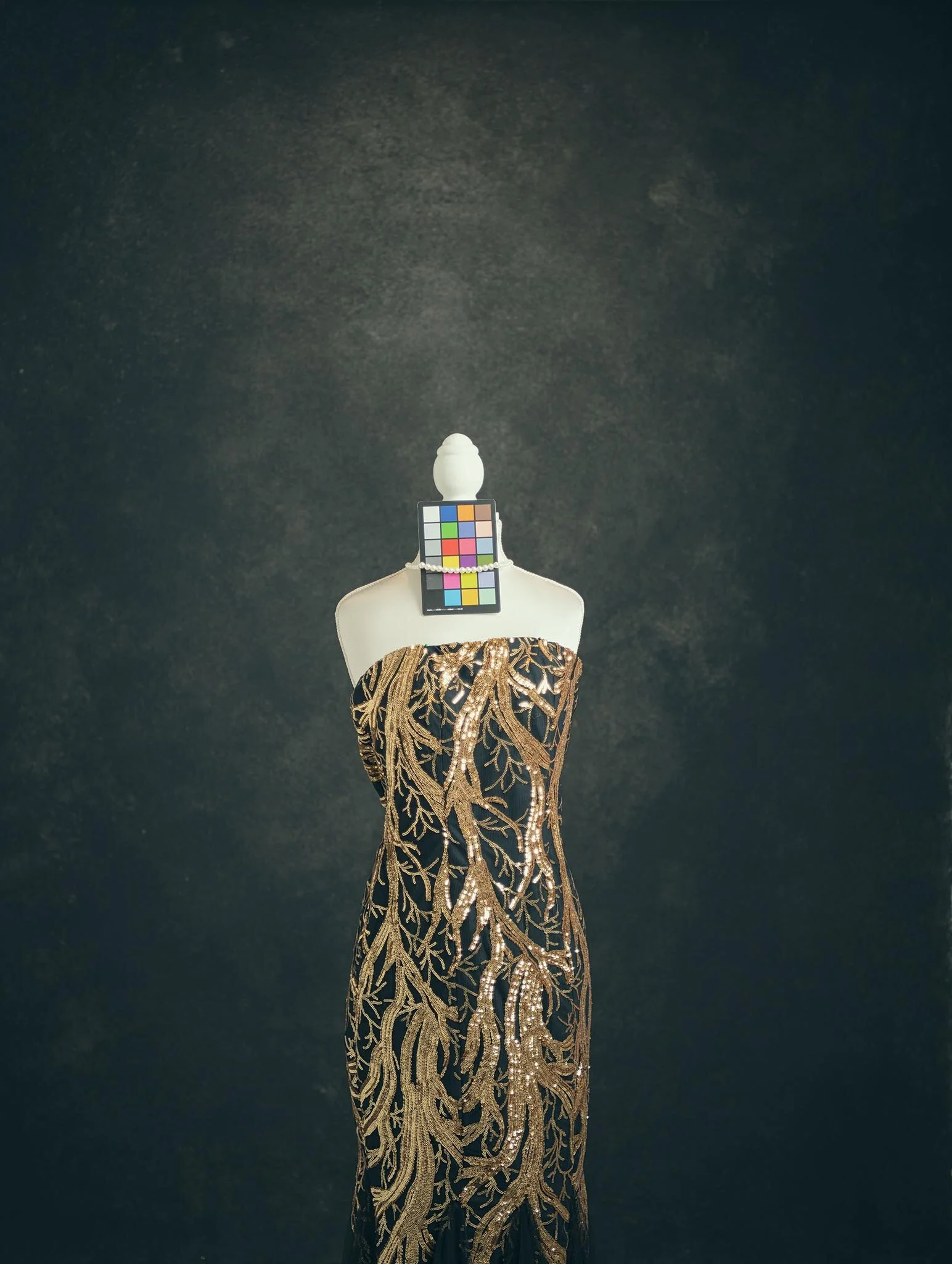 Black dress with gold embroidery on a mannequin against a dark background.