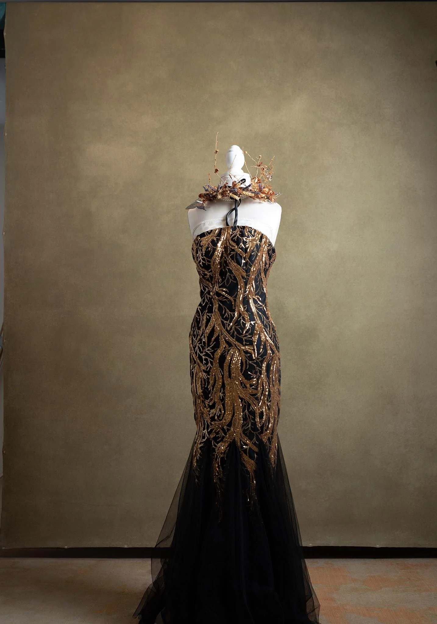 Black evening gown with gold embroidered leaf pattern displayed on a mannequin against a beige background.