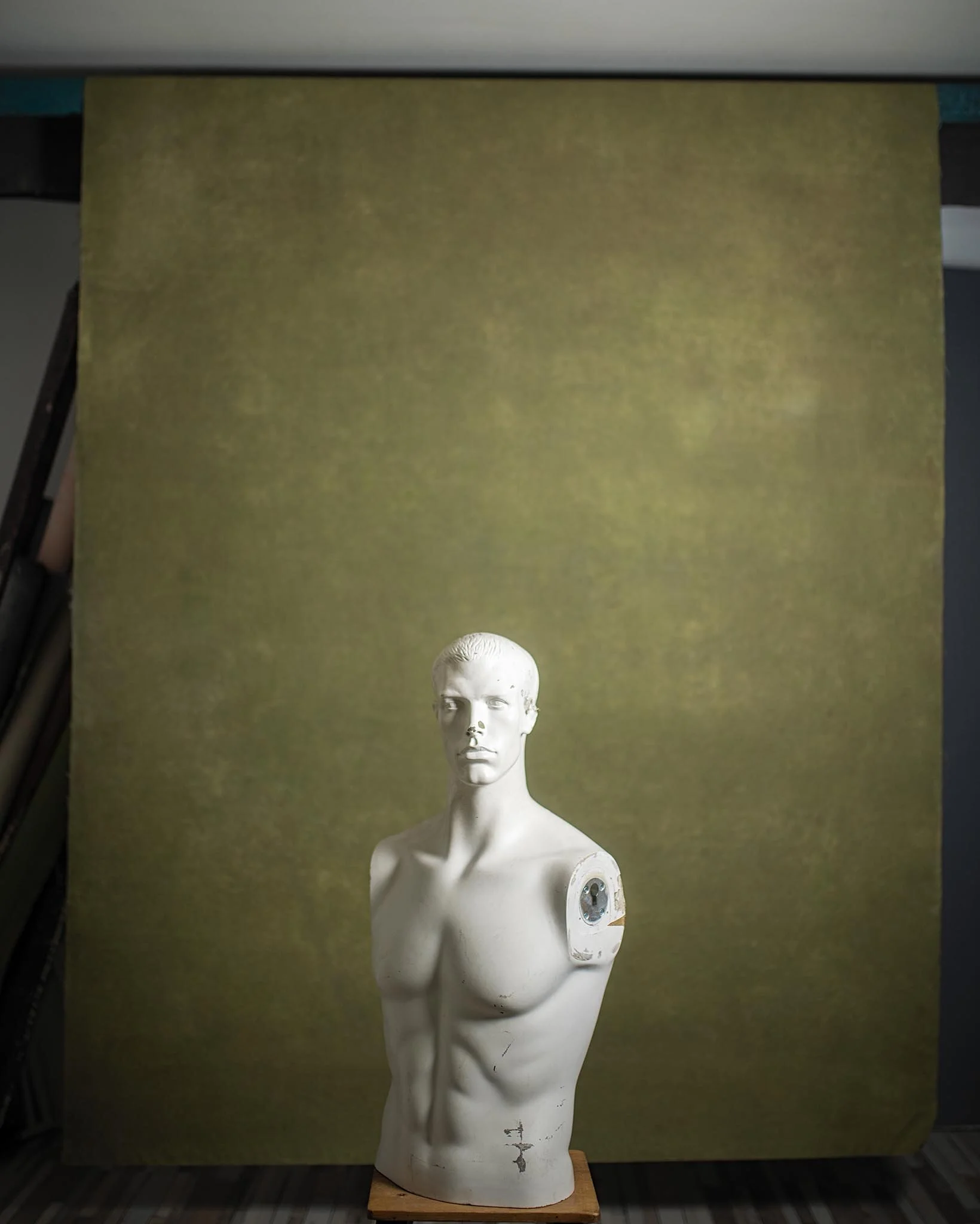 A white mannequin bust with a male torso, missing its left arm, placed in front of a greenish backdrop.