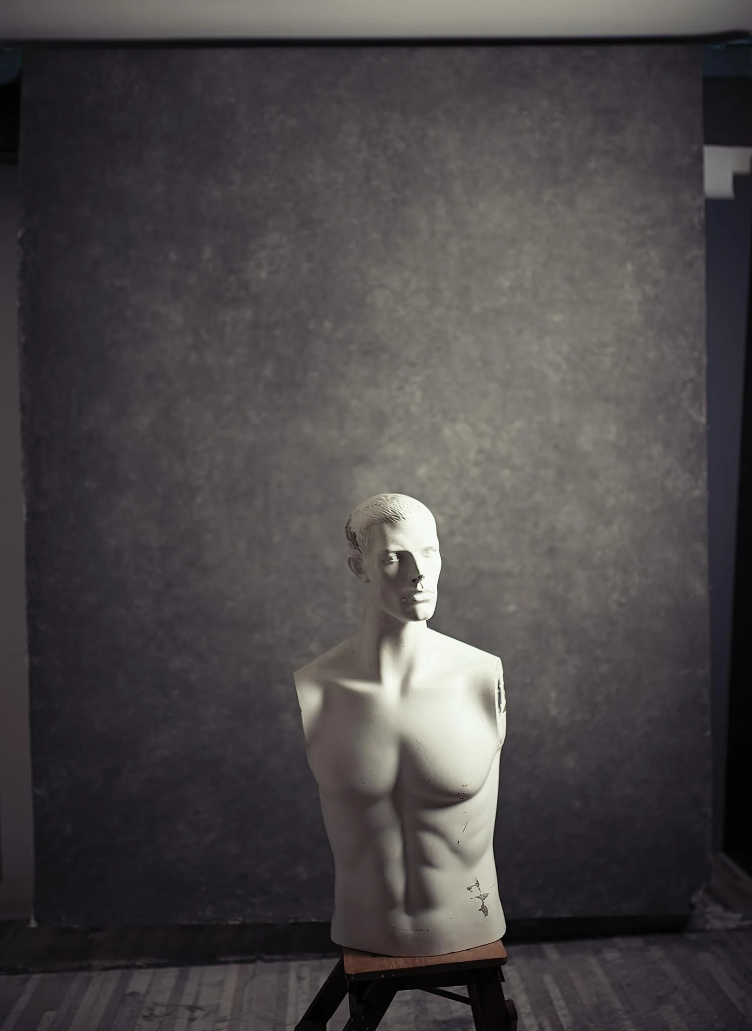 White female torso bust sculpture of a woman with a short hairstyle, placed on a small wooden stand against a dark plain background.