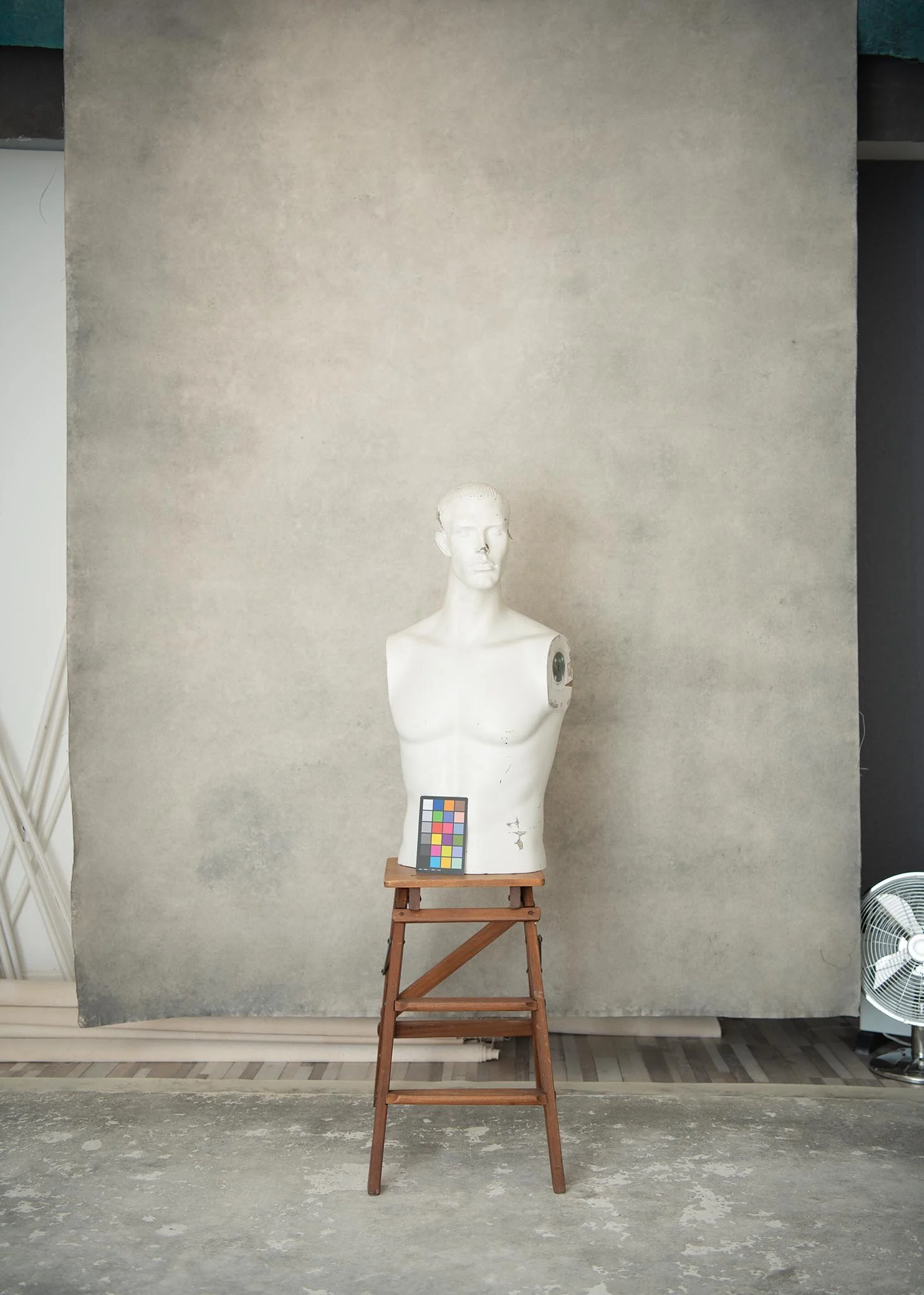A mannequin bust with a color calibration card placed on a wooden stool, set against a plain backdrop in a studio.
