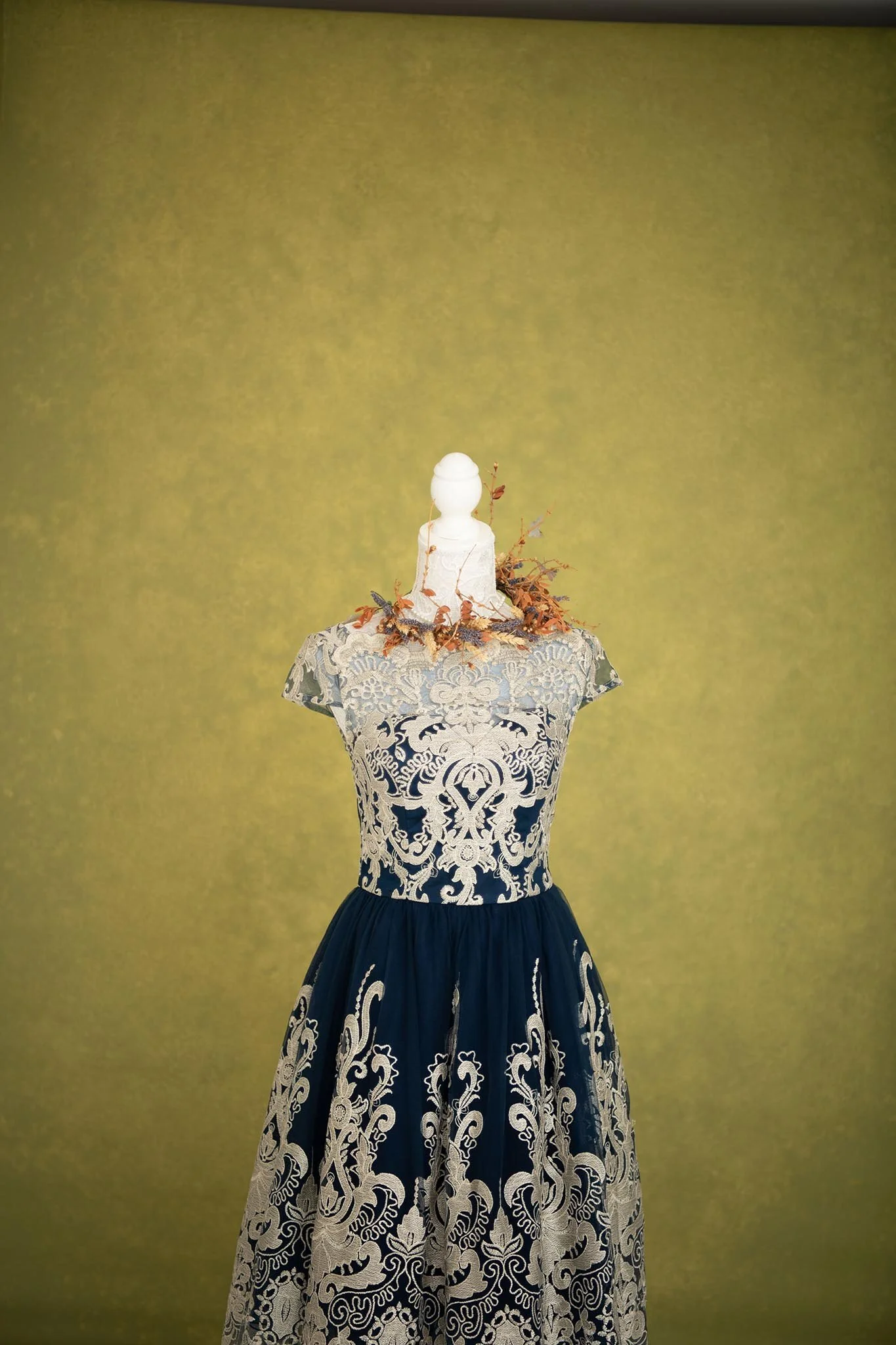 A black and white embroidered gown displayed on a mannequin with an olive green background.