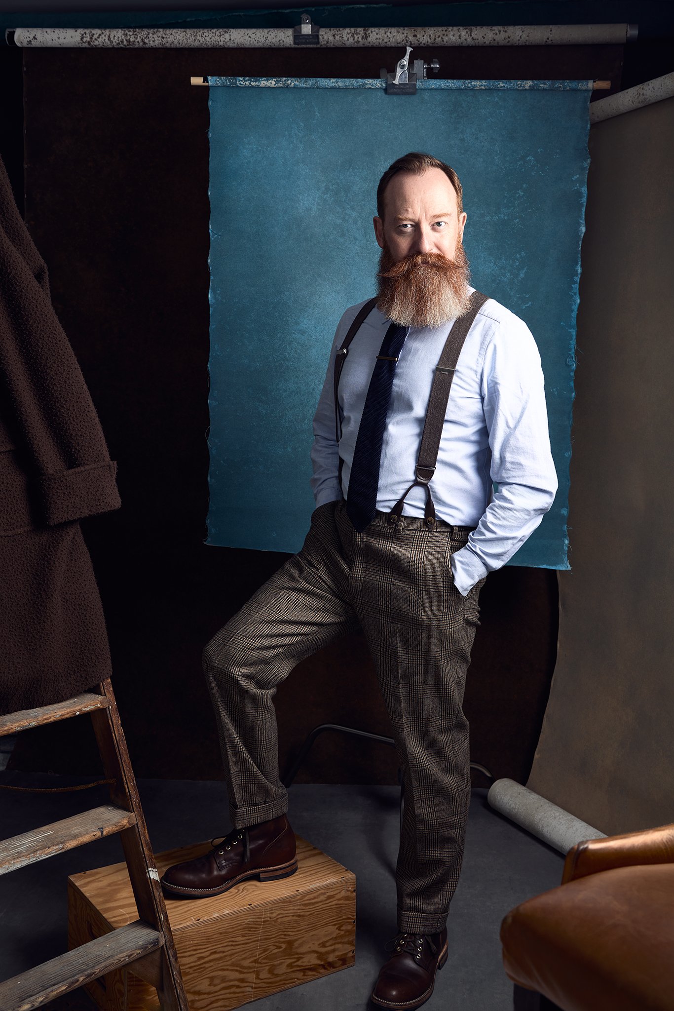 Andy Sinclair studio portrait - bearded man in braces against a teal blue hand painted canvas backdrop by Hand Painted Backdrops UK.