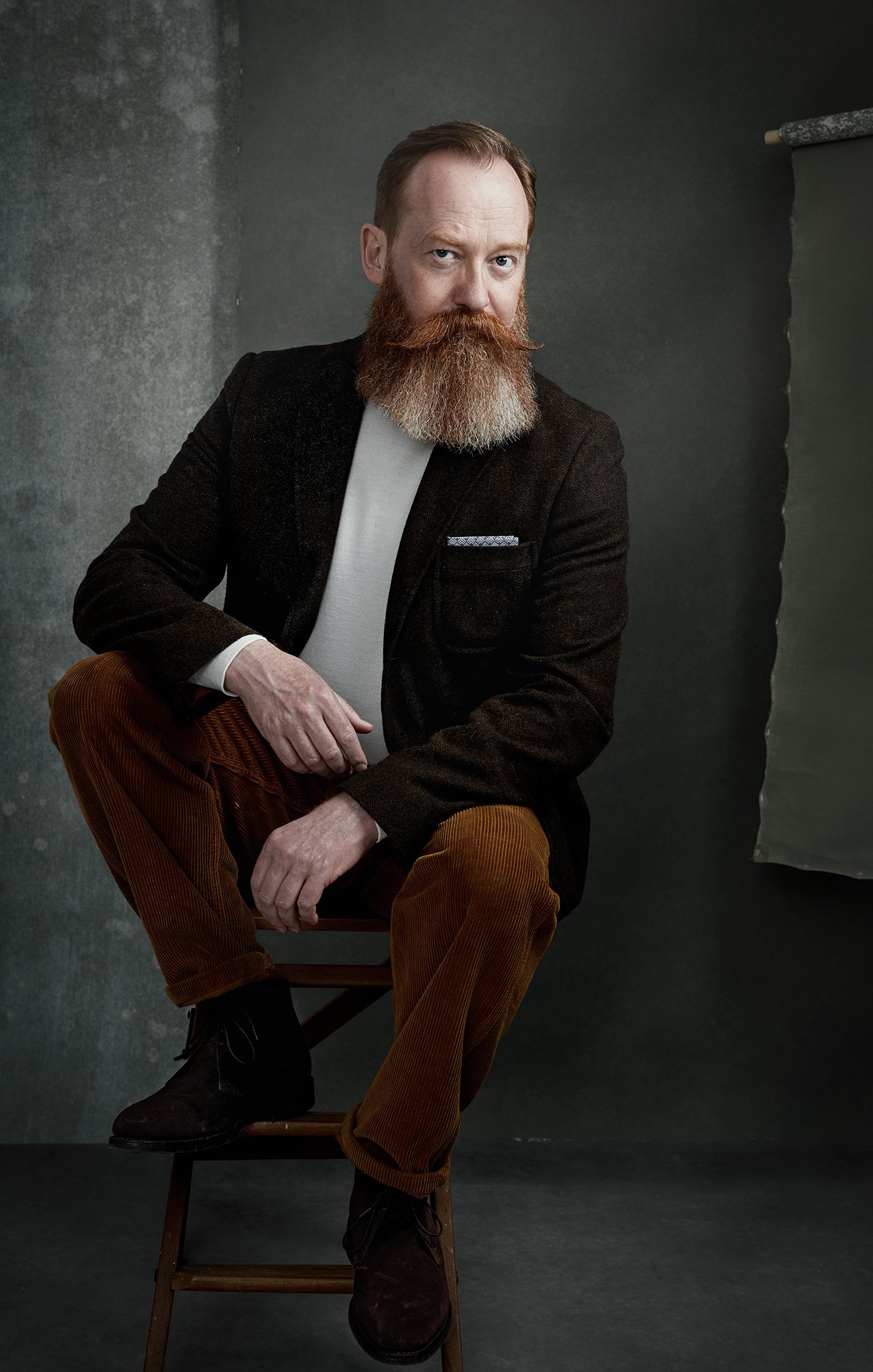 Andy Sinclair close-up portrait - bearded man in a dark jacket against a grey textured hand painted canvas backdrop by Hand Painted Backdrops UK.