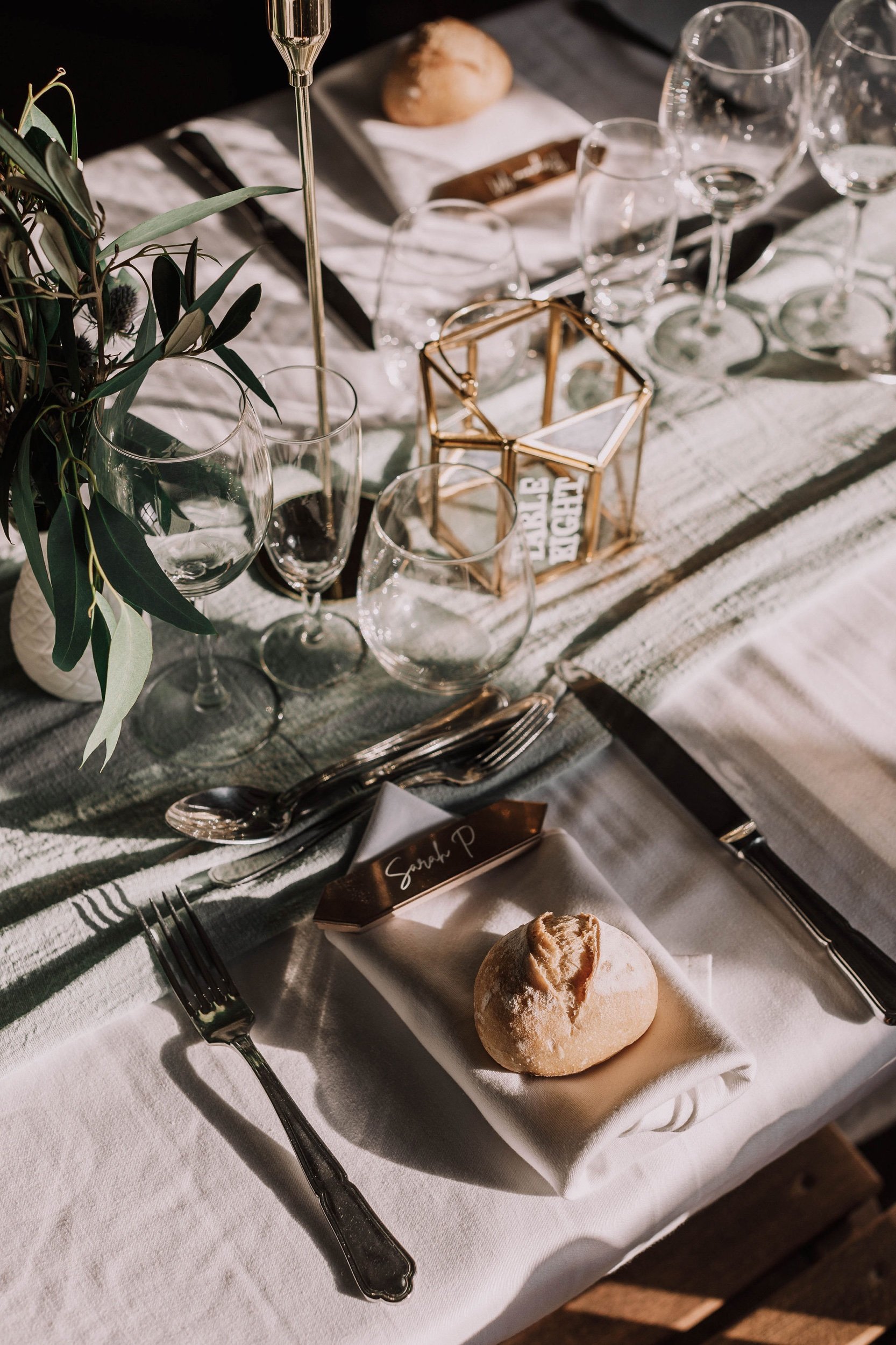 Table dressée avec des verres, des couverts, du pain, des serviettes en tissu et une décoration florale.