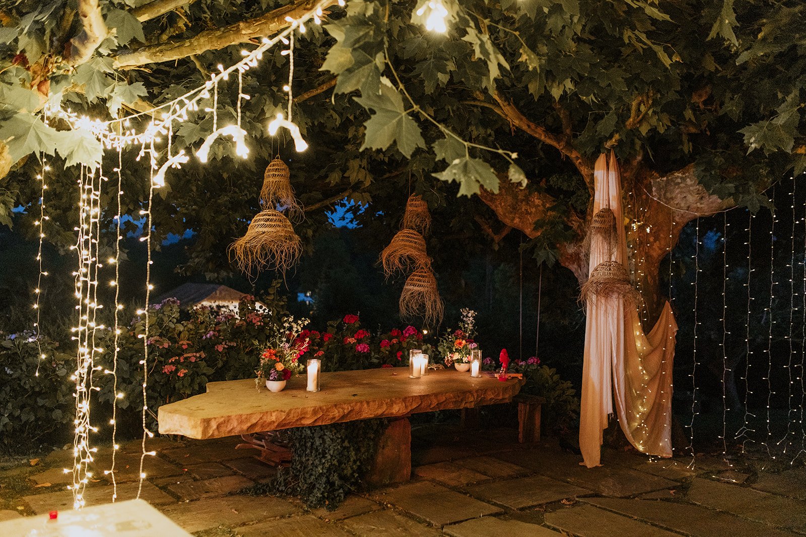 Table en bois sous un arbre avec guirlandes lumineuses et décorations végétales.
