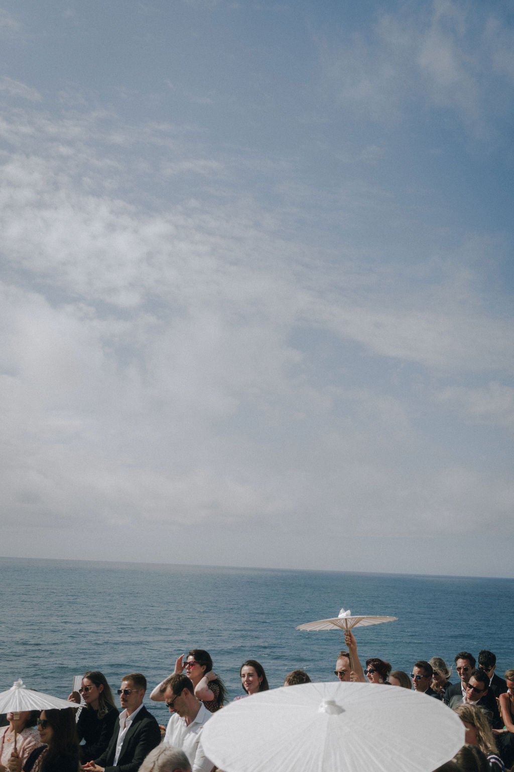 Groupe de personnes avec des ombrelles blanches près de la mer sous un ciel partiellement nuageux.
