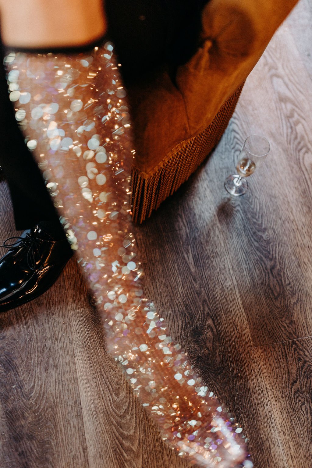 Jambe en collants à paillettes près d'un fauteuil, verre à champagne sur le sol.