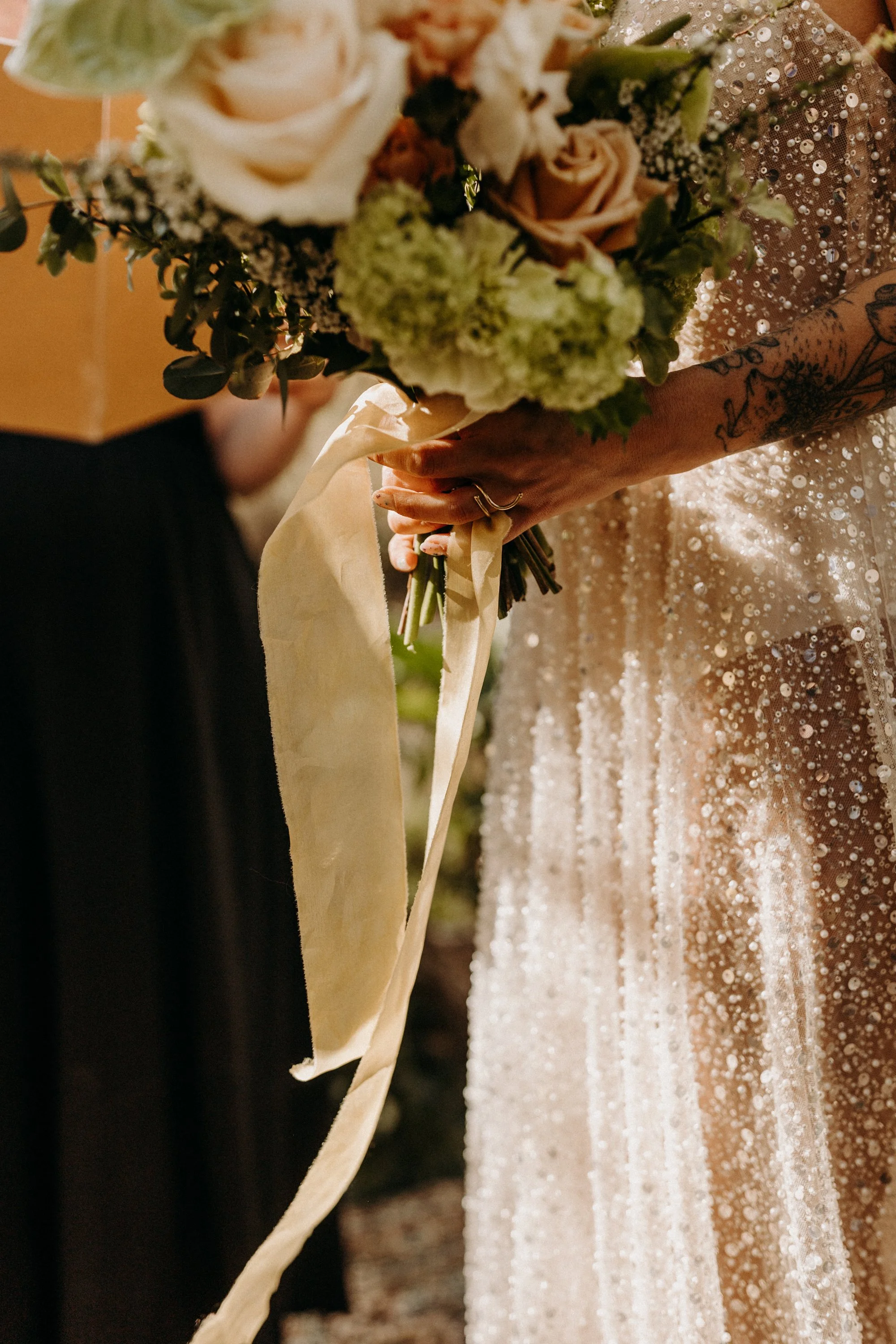 Une personne en robe de mariée tient un bouquet de fleurs avec un ruban long, lors de la cérémonie de mariage.