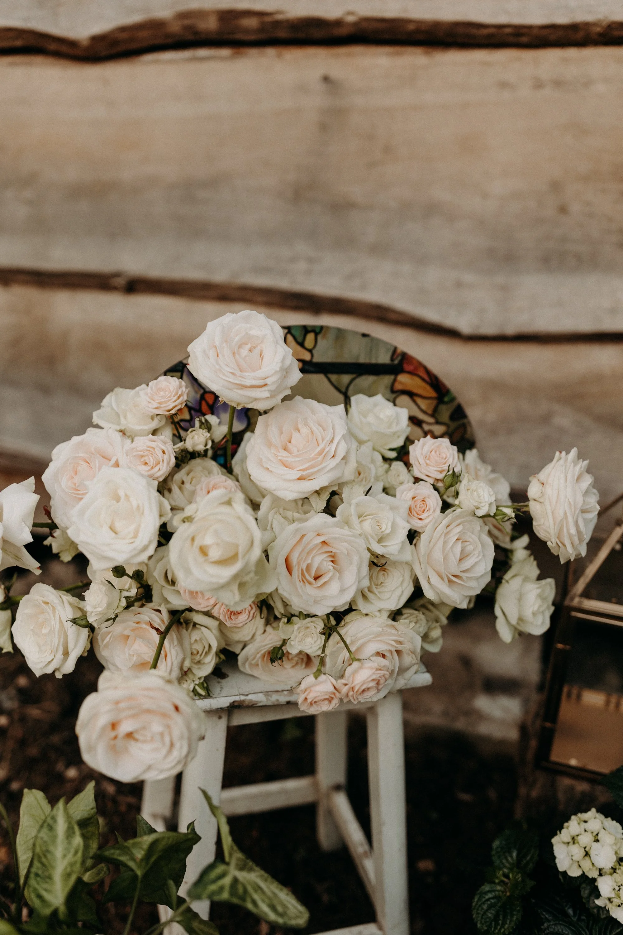 Bouquet de roses blanches et roses pâles posées sur un petit tabouret blanc en bois, avec un décor en bois en arrière-plan.