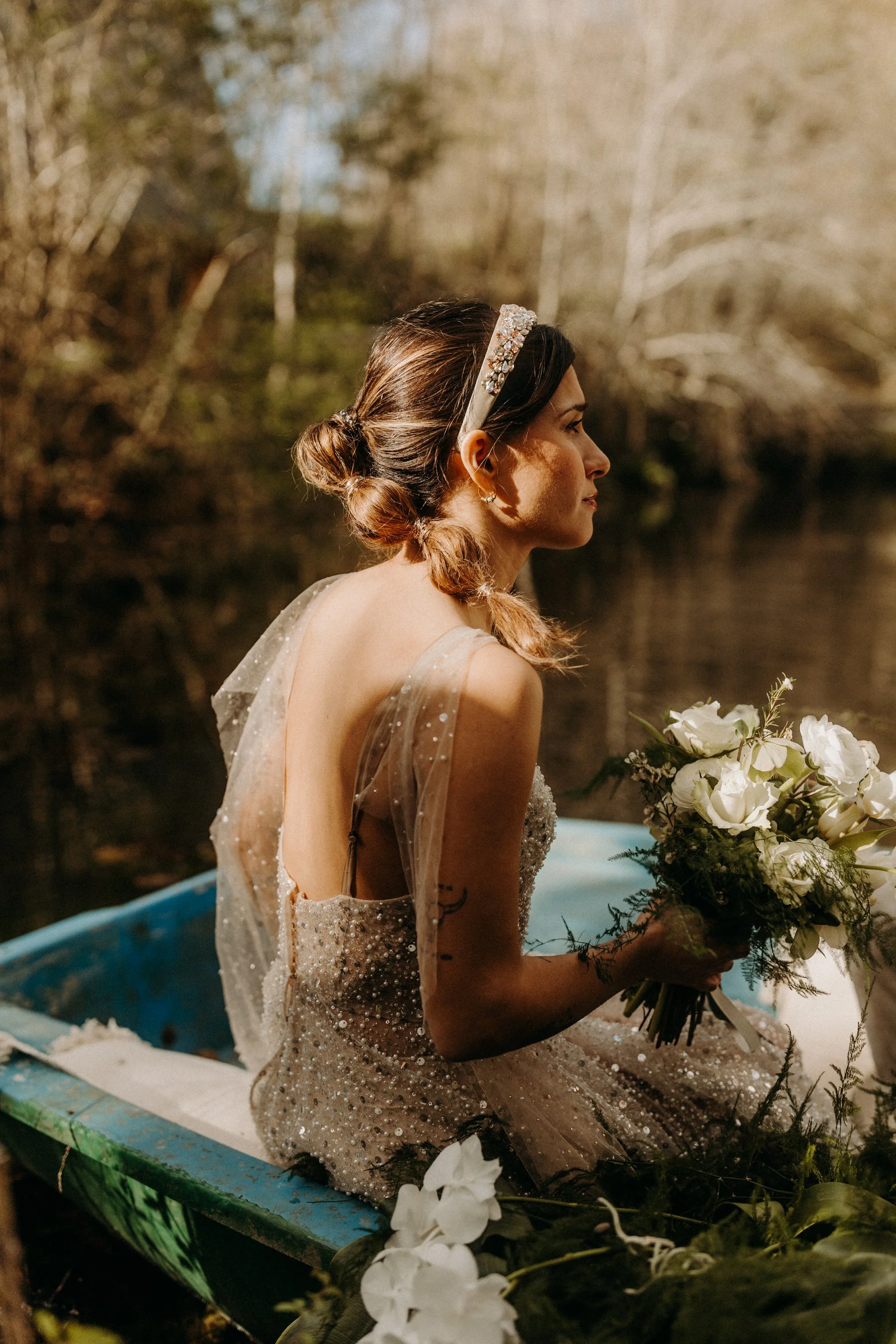 Femme tenant un bouquet de fleurs, assise dans une petite barque, en robe élégante, près d'une rivière en pleine nature.