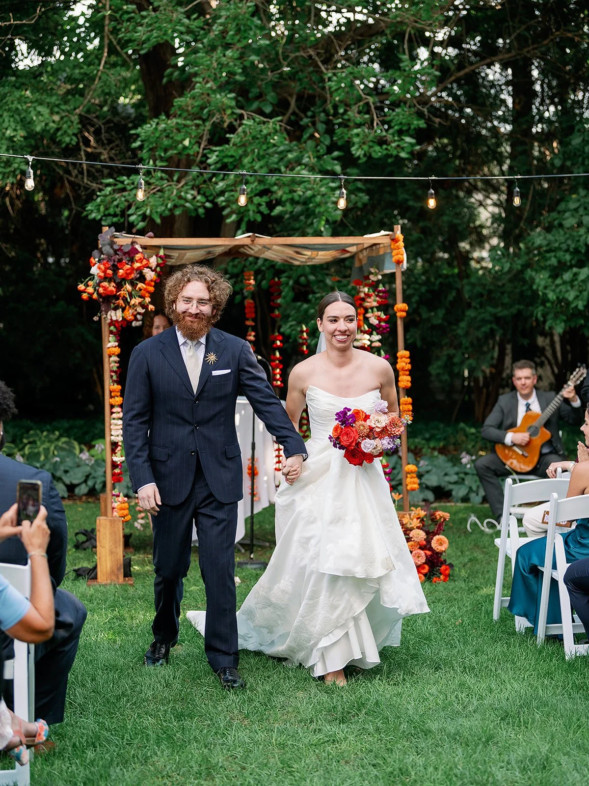 recently married couple walking down the aisle with colorful chuppah in the background