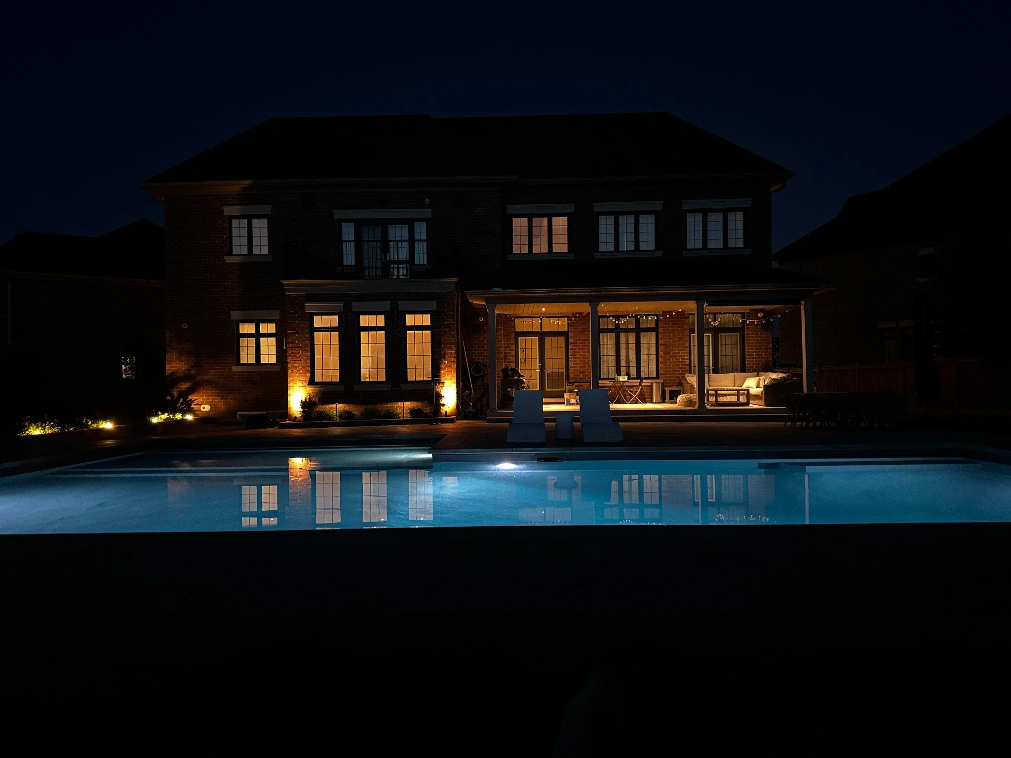 Custom brick home at night with illuminated windows, covered patio and swimming pool.