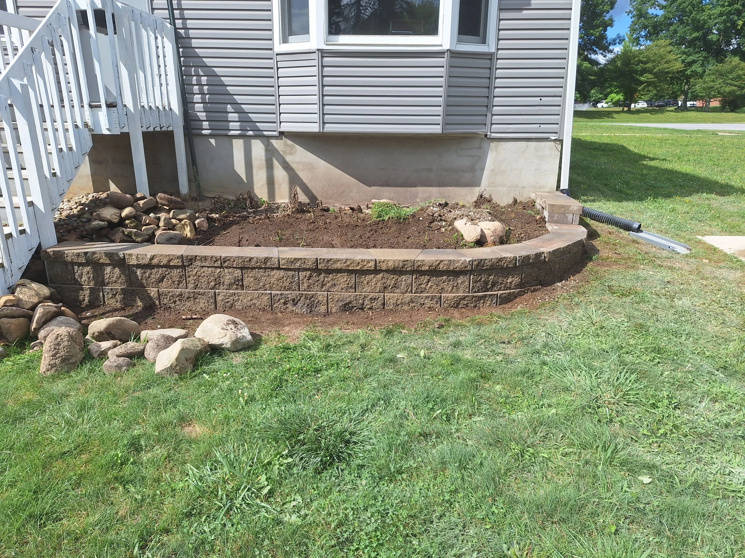 Front yard with a new brick flower bed, rocks, and a small set of stairs on the left.