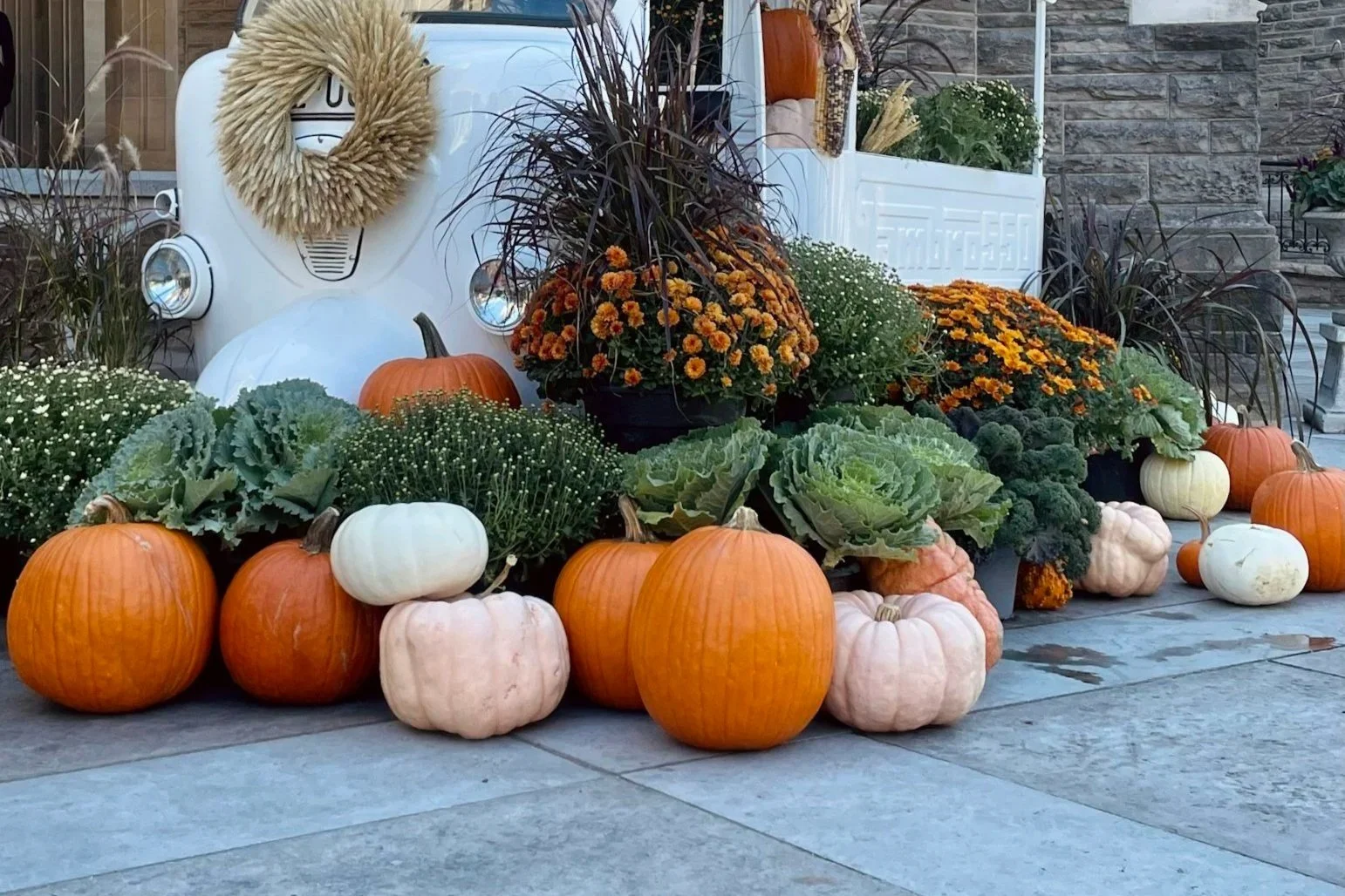 Pumpkins and fall flowers surrounding a white vintage basket on a porch.