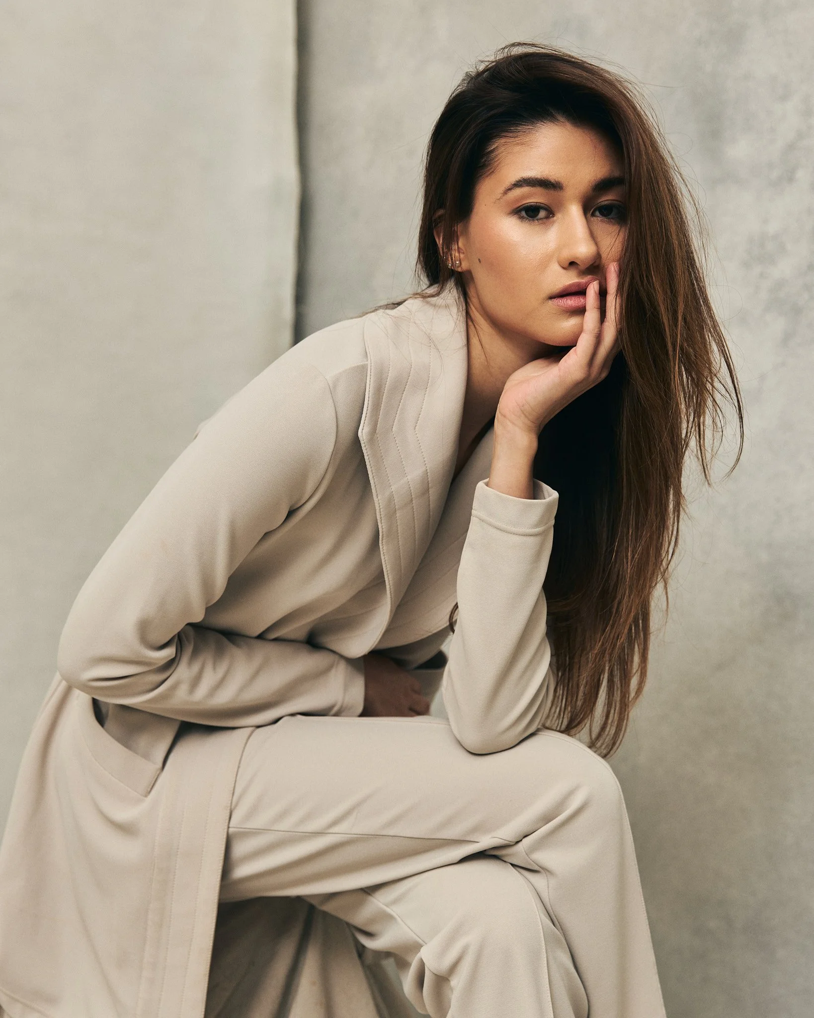Woman in beige outfit with long hair, sitting against a neutral background.