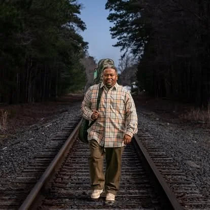 Outdoor portrait of a man in a patterned jacket standing on railway tracks.