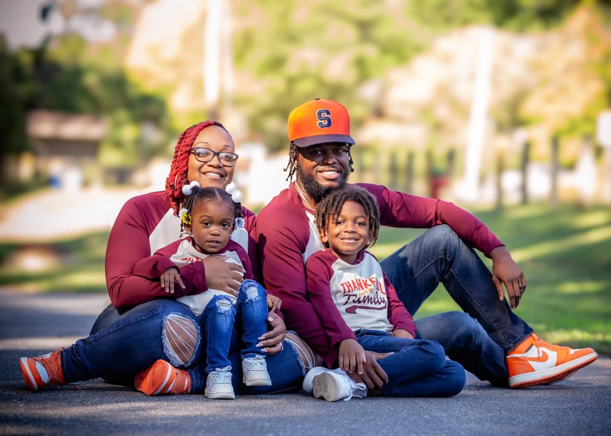 Family of four smiling together outdoors in coordinated burgundy tops.