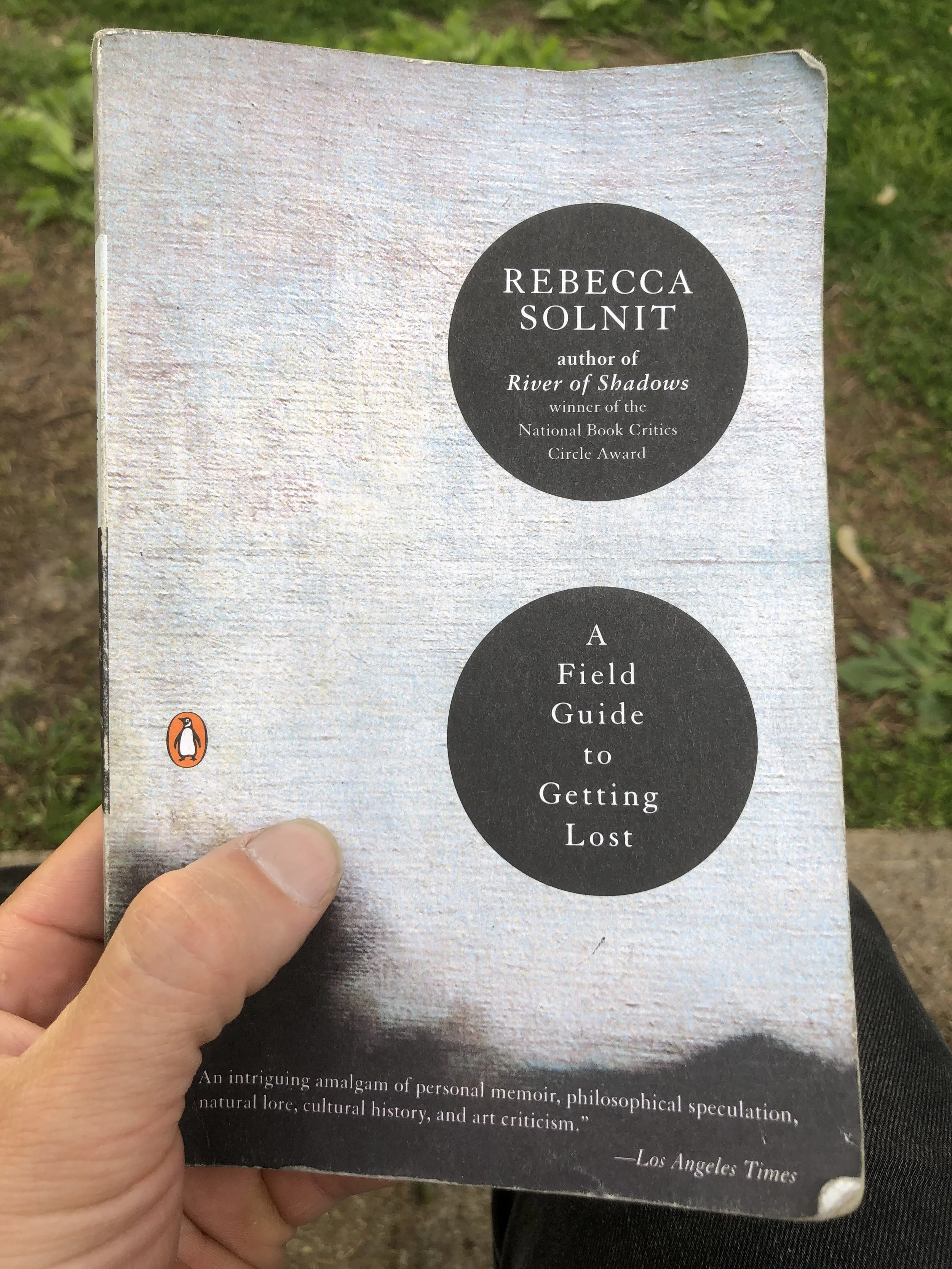 A hand holding a copy of Rebecca Sonit's book A Field Guide to Getting Lost