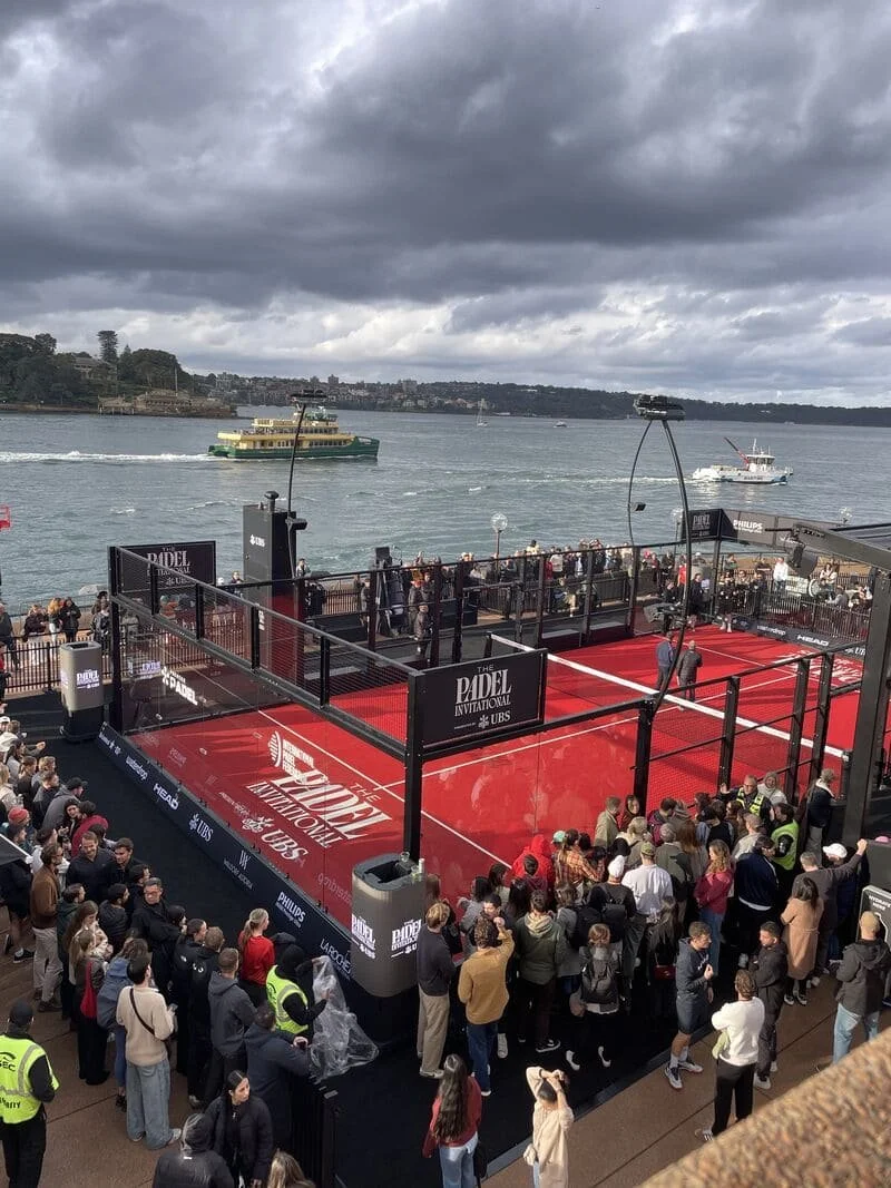 Crowds around the red padel court on the Sydney Opera House’s Northern Broadwalk, with a ferry crossing Sydney Harbour behind