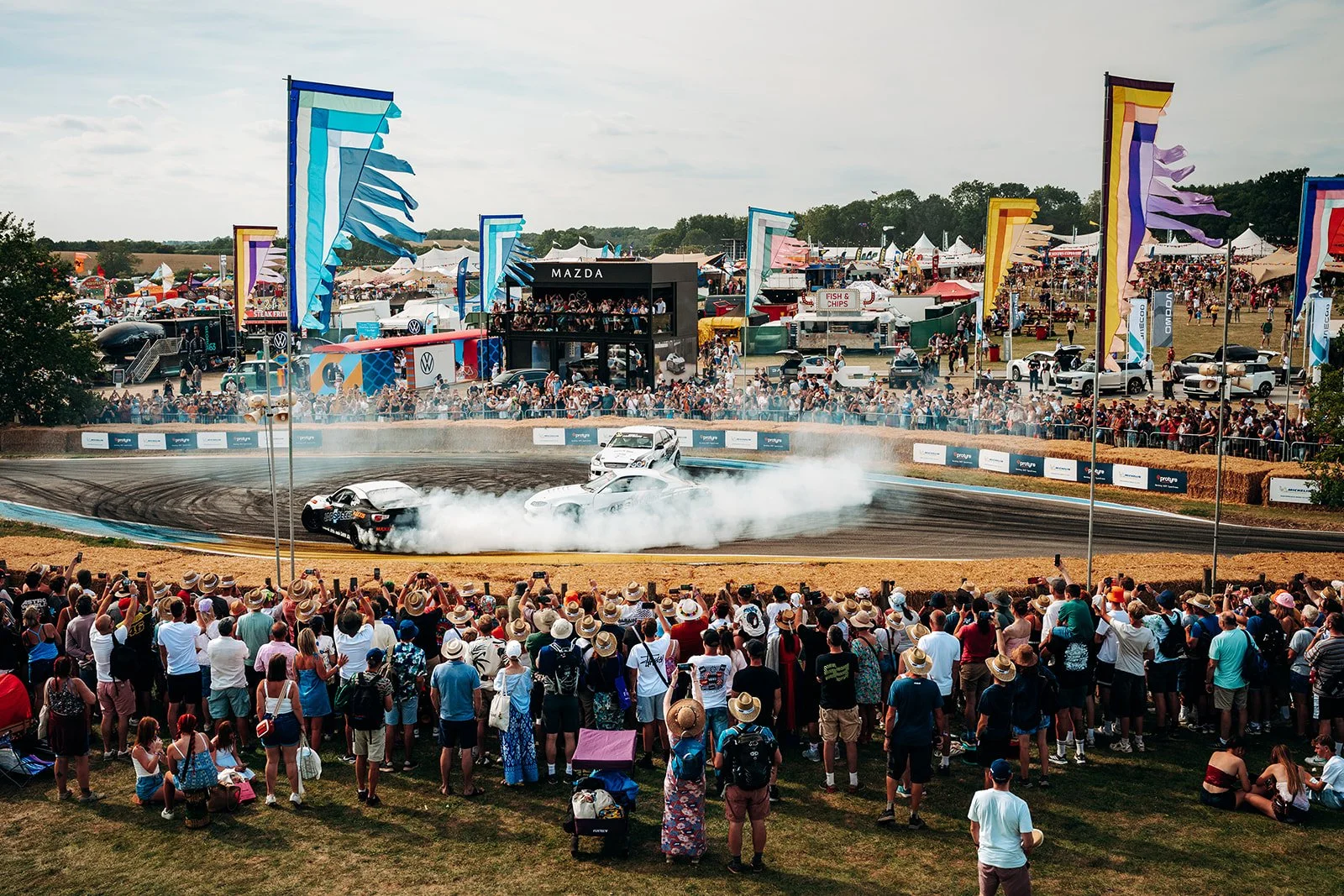 Two cars drifting side by side in front of a large crowd at CarFest