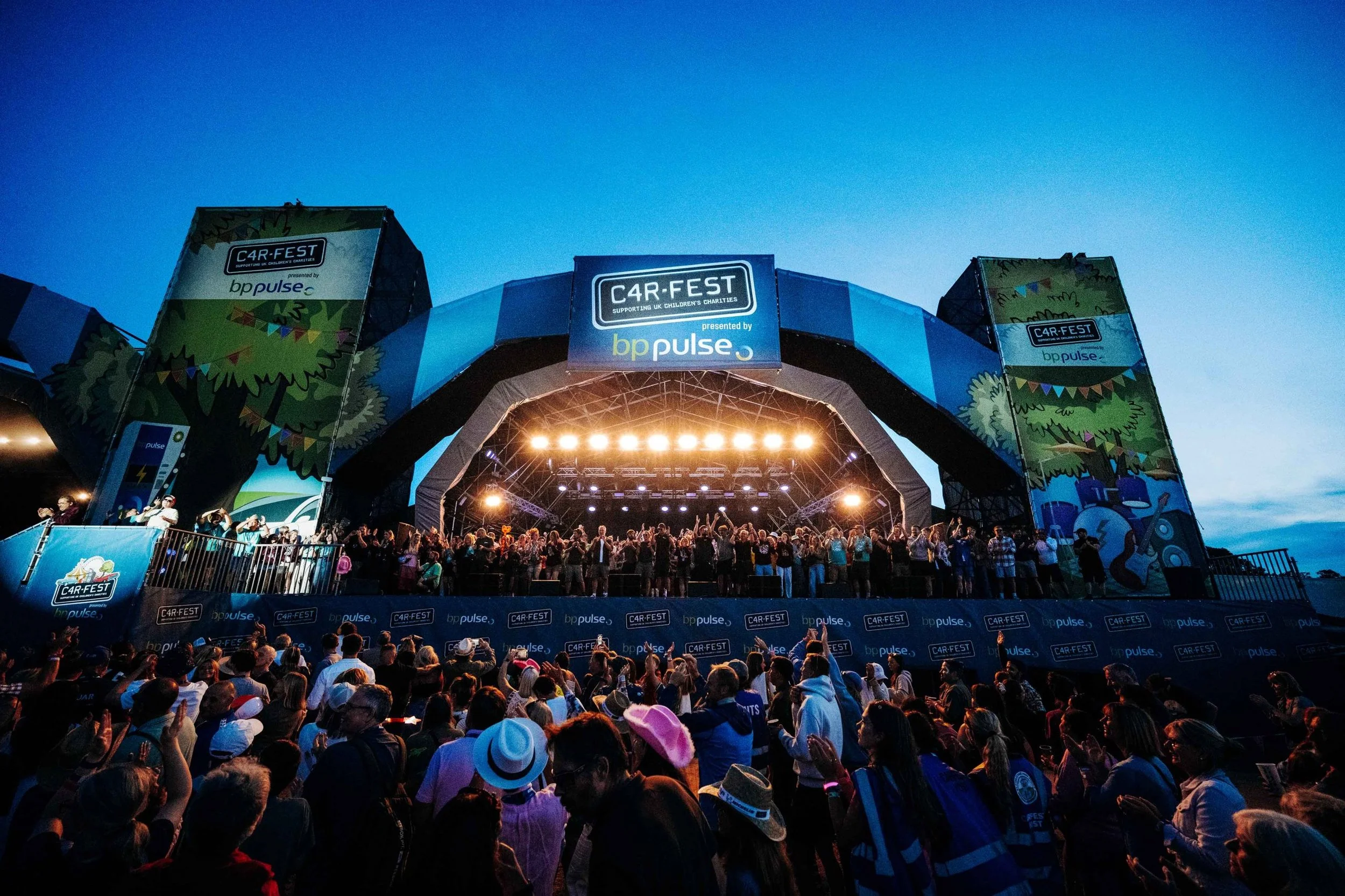 Crowd cheering in front of the CarFest main stage at dusk