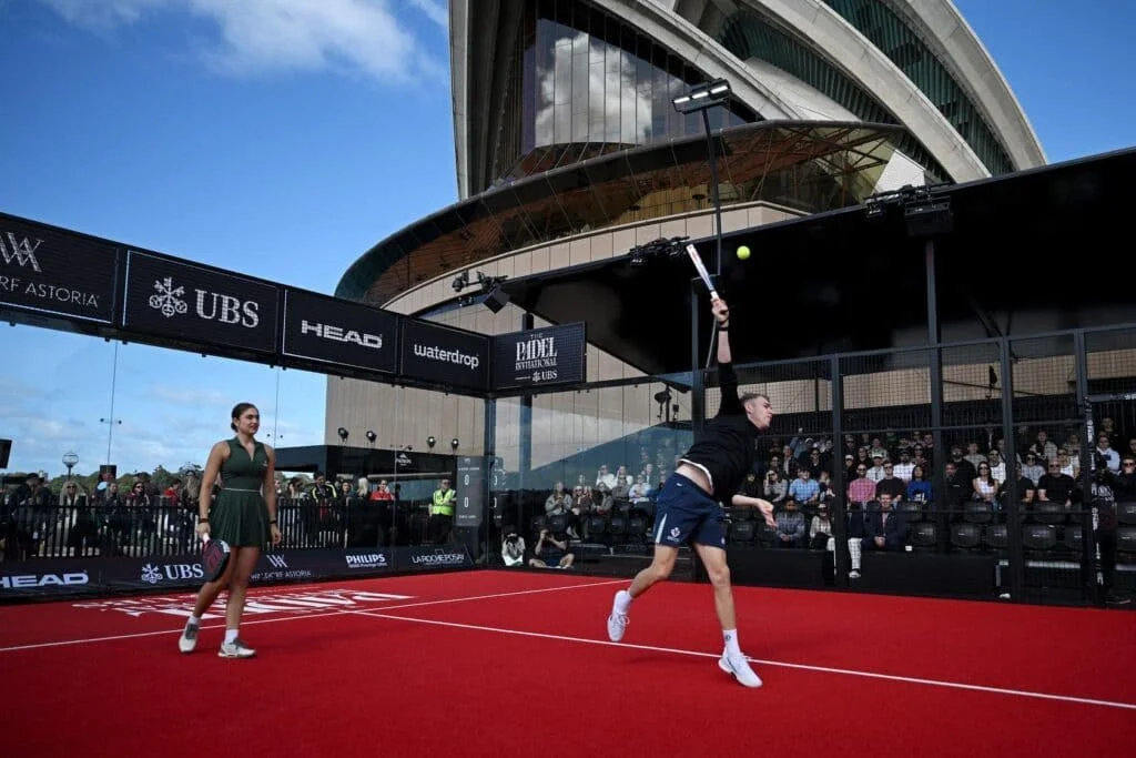 Player hitting an overhead shot during a padel exhibition match beside the Sydney Opera House