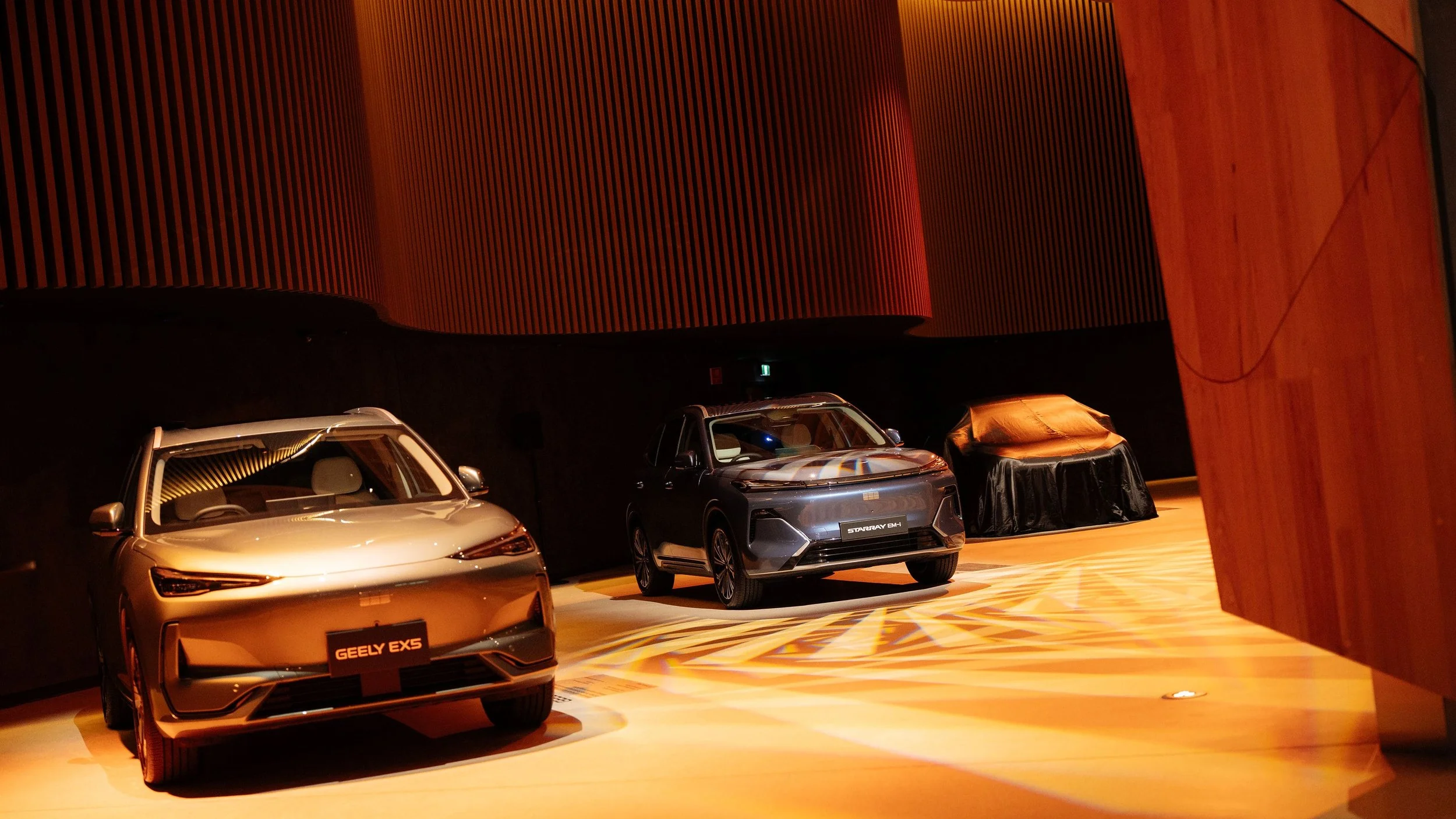 Geely EX5 and Starray EM-i cars on display at The Cutaway, Sydney, with a covered vehicle waiting to be revealed