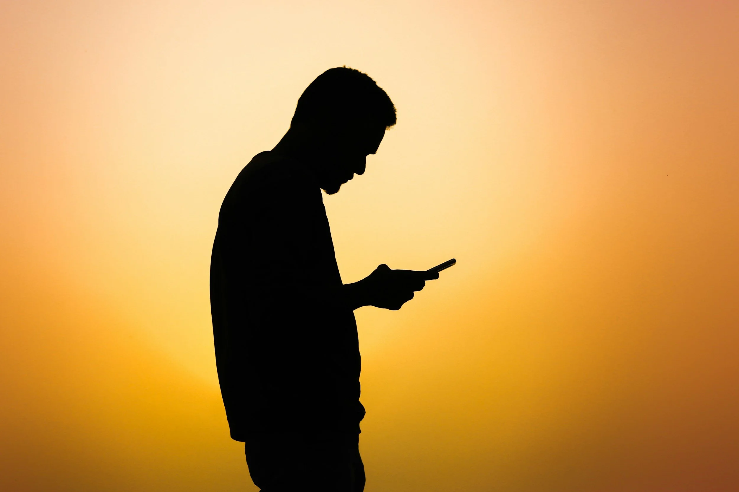 Silhouette of a person looking at their phone during sunset, representing reflection and trauma-informed healing.