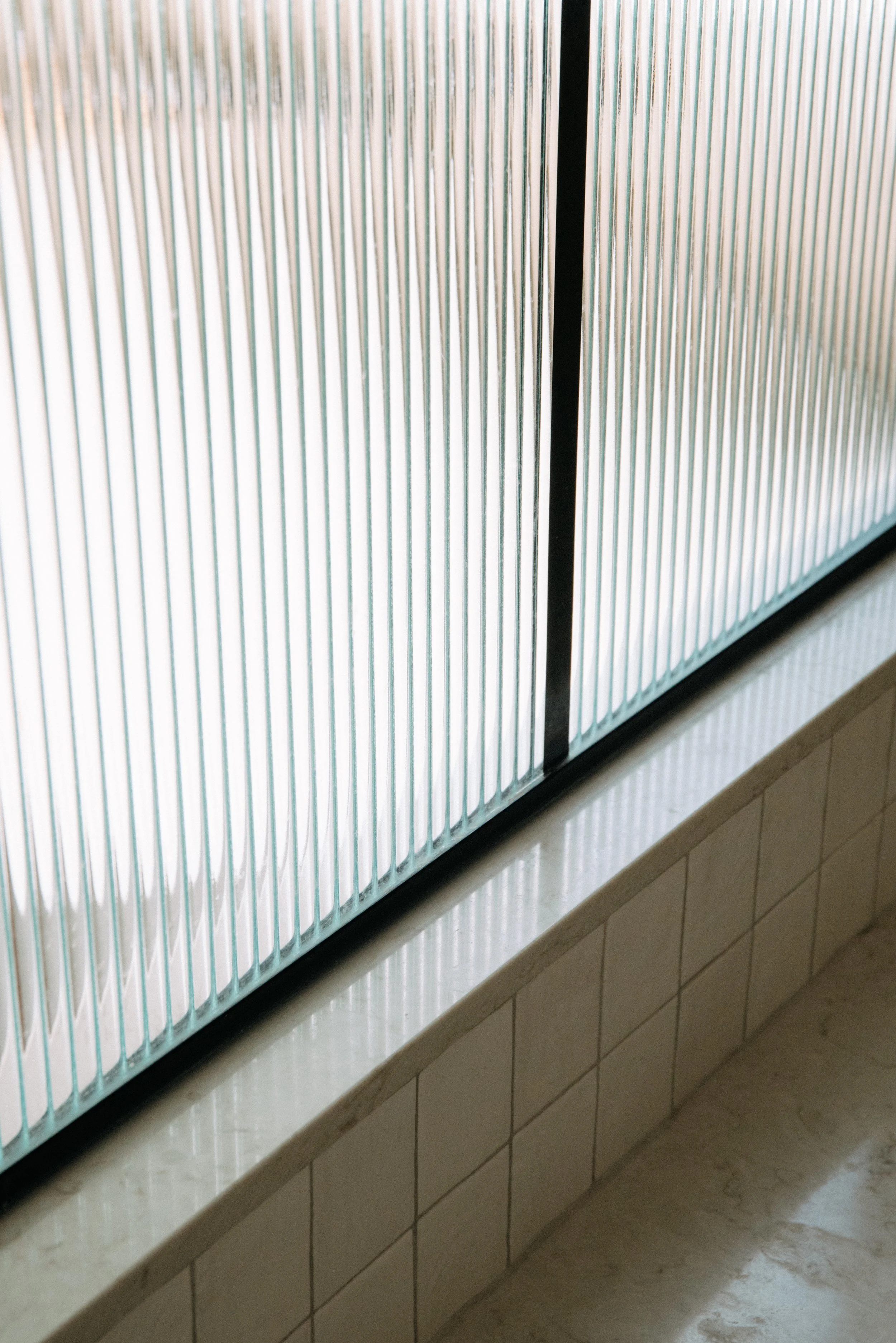 Close-up of a textured glass window with vertical ridges, mounted on a tiled wall.
