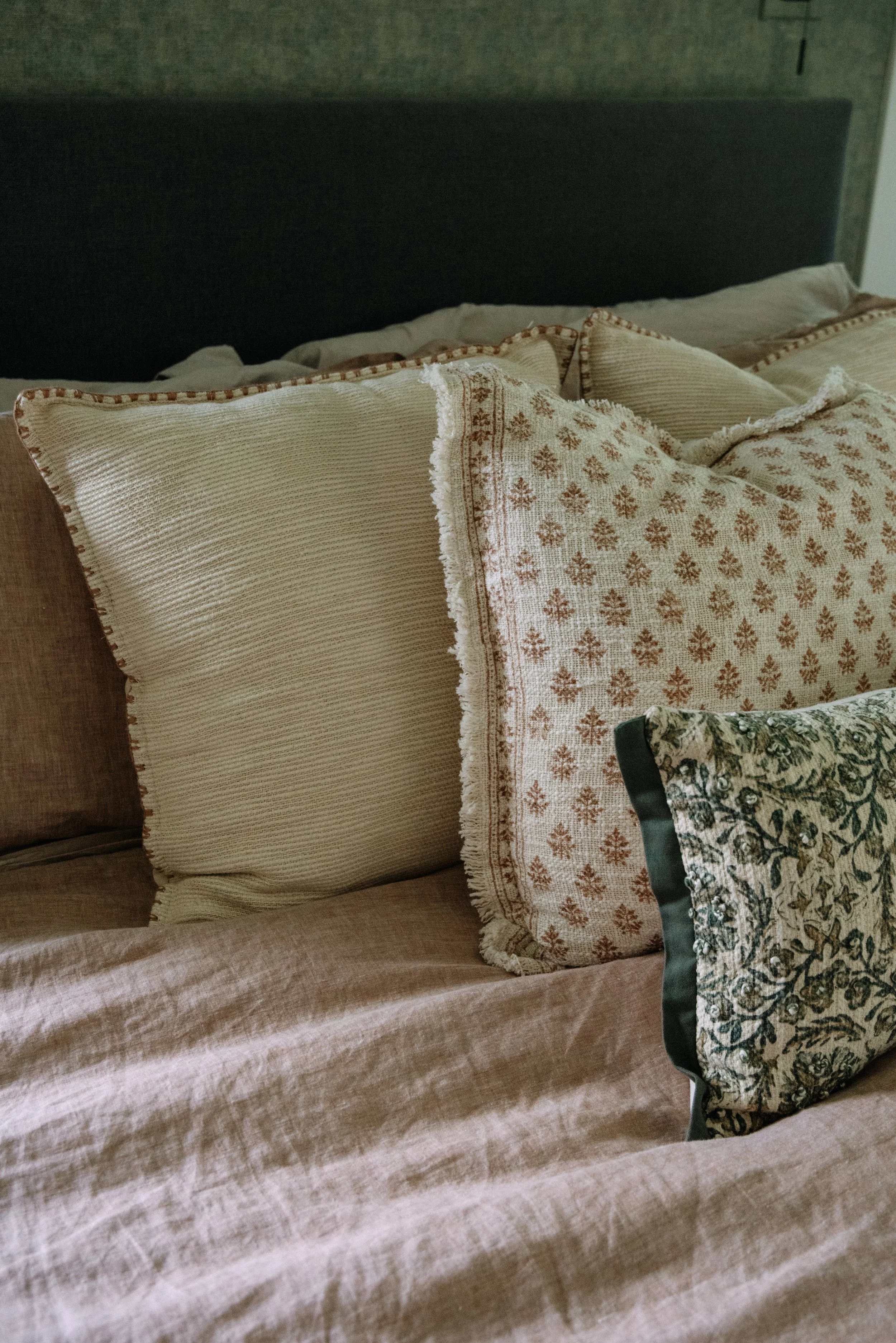 Close-up of a neatly made bed with multiple decorative pillows featuring various patterns and textures, in a cozy bedroom setting.