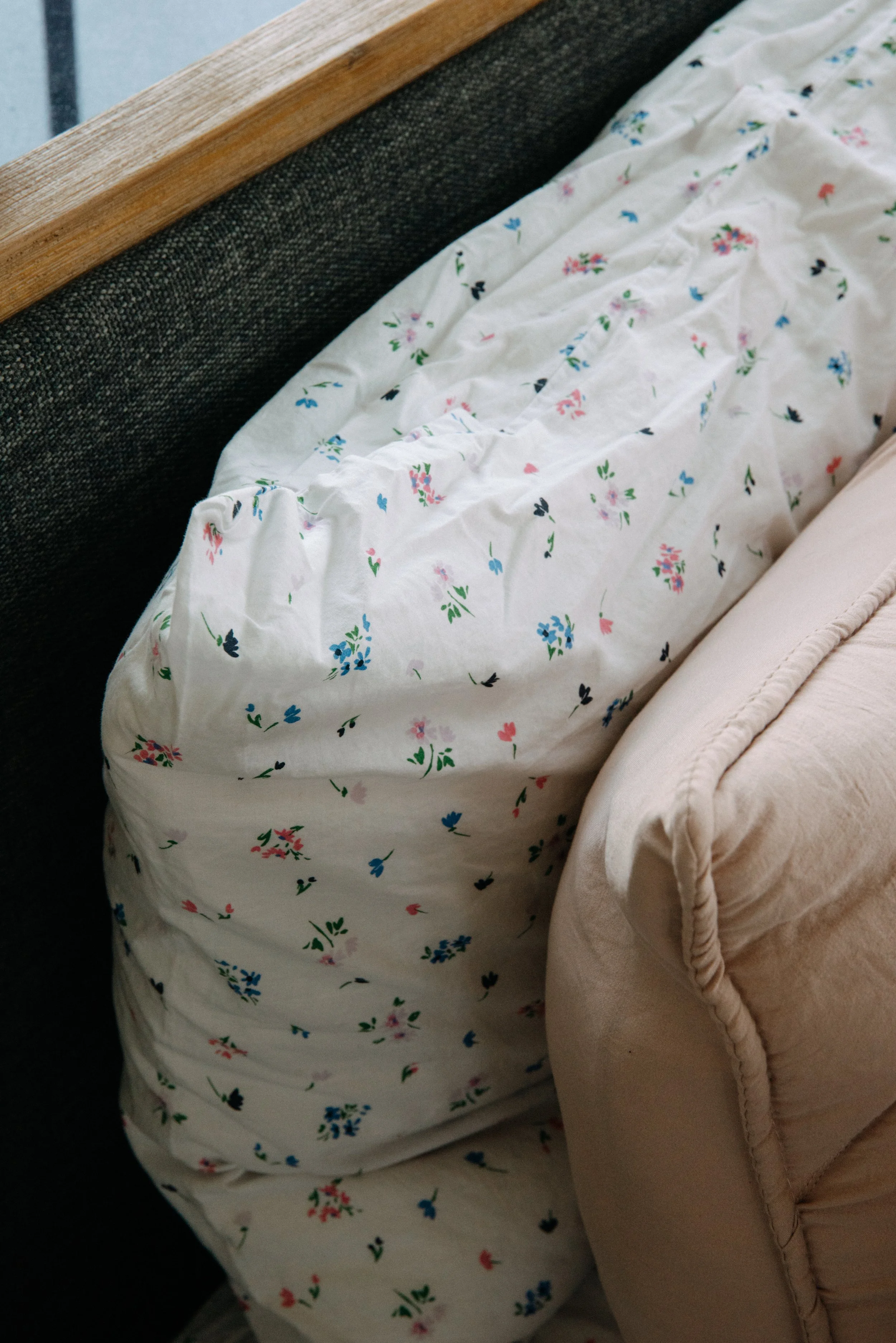 Close-up of a floral-patterned fabric draped over a piece of furniture, with a beige upholstered armrest visible to the right.