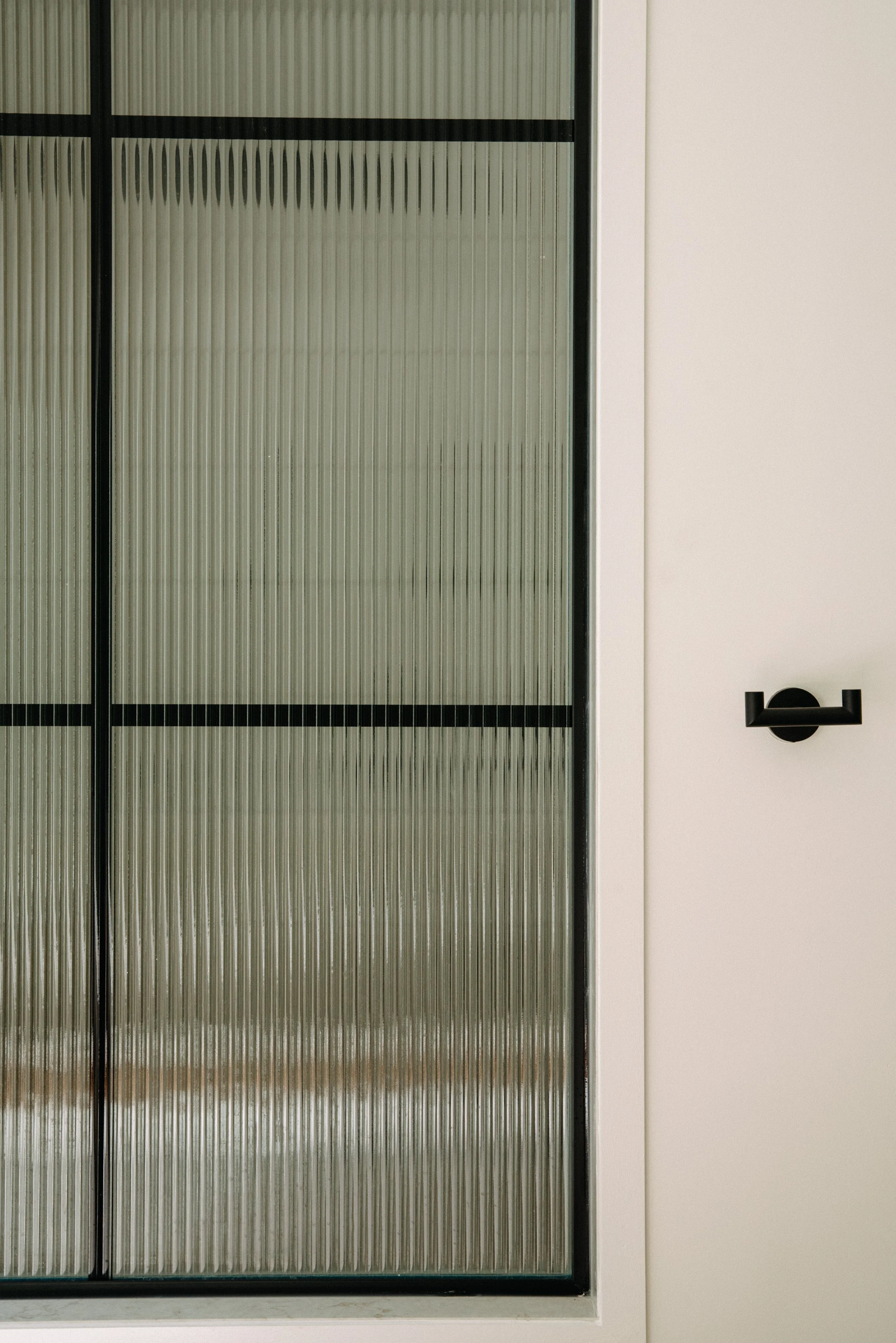 A glass door with a black frame and textured glass panels next to a white wall with a black wall hook.