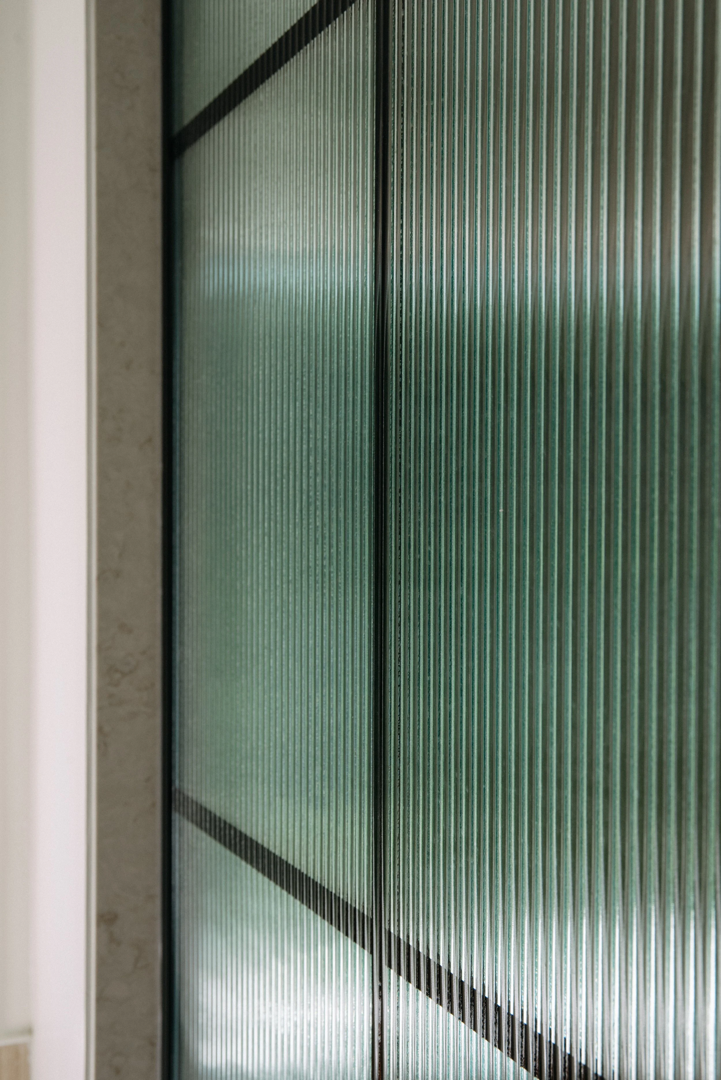 Close-up of glass sliding closet doors with a ribbed textured surface and black trim, reflecting light.