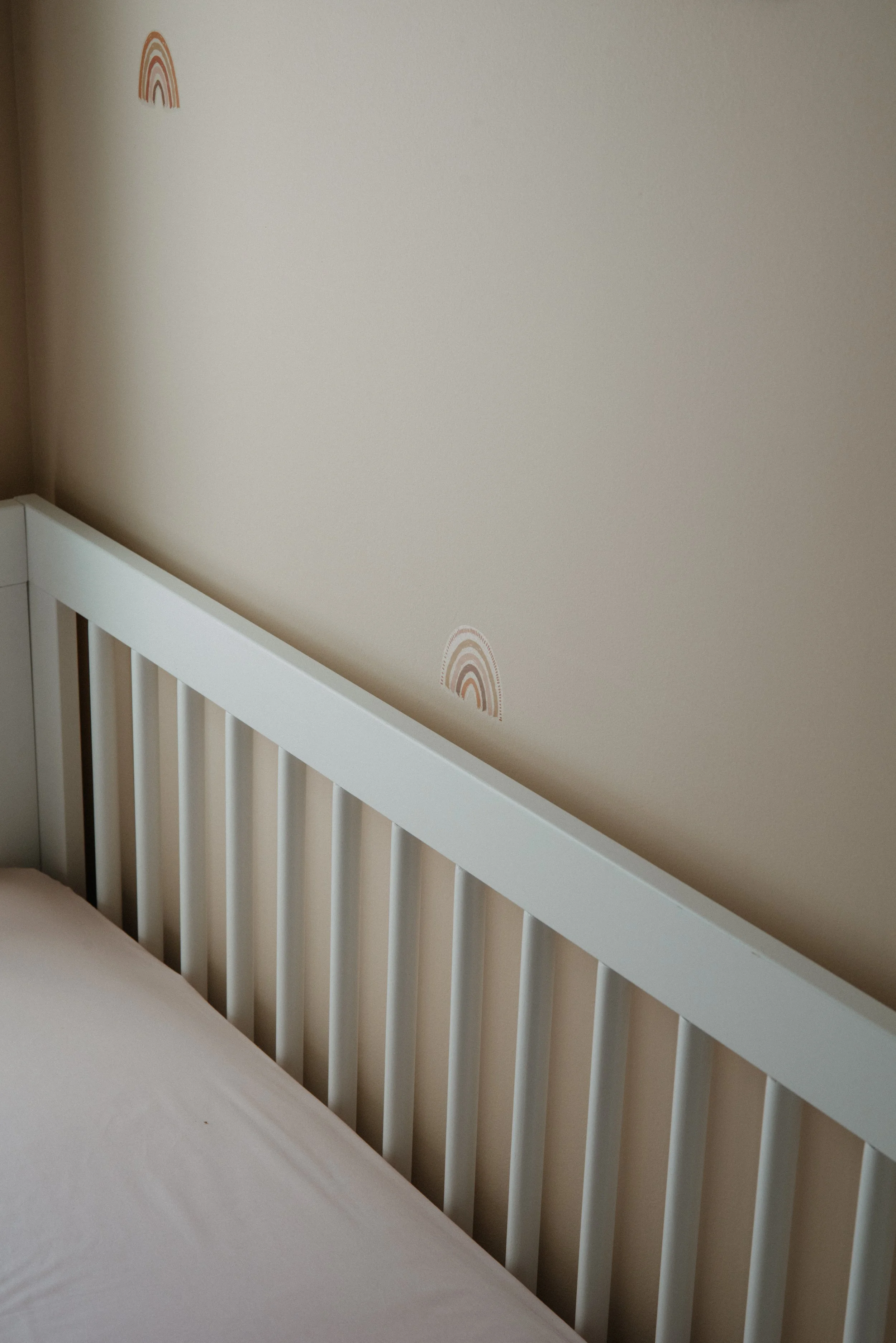 Close-up of a white crib and beige wall with small rainbow decals.