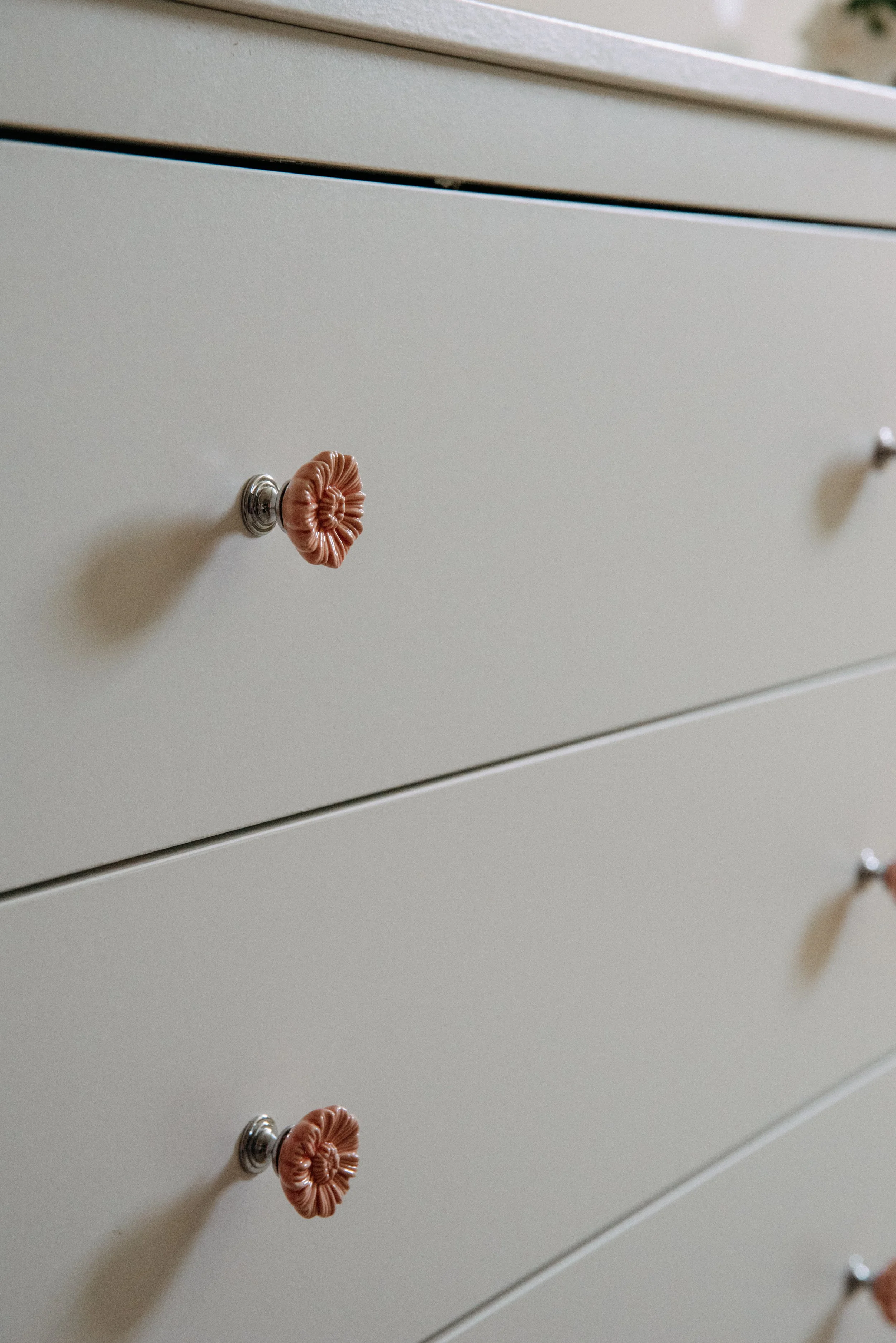 Close-up of a light-colored dresser with decorative round knobs, featuring an orange-brown ceramic or fabric flower detail.