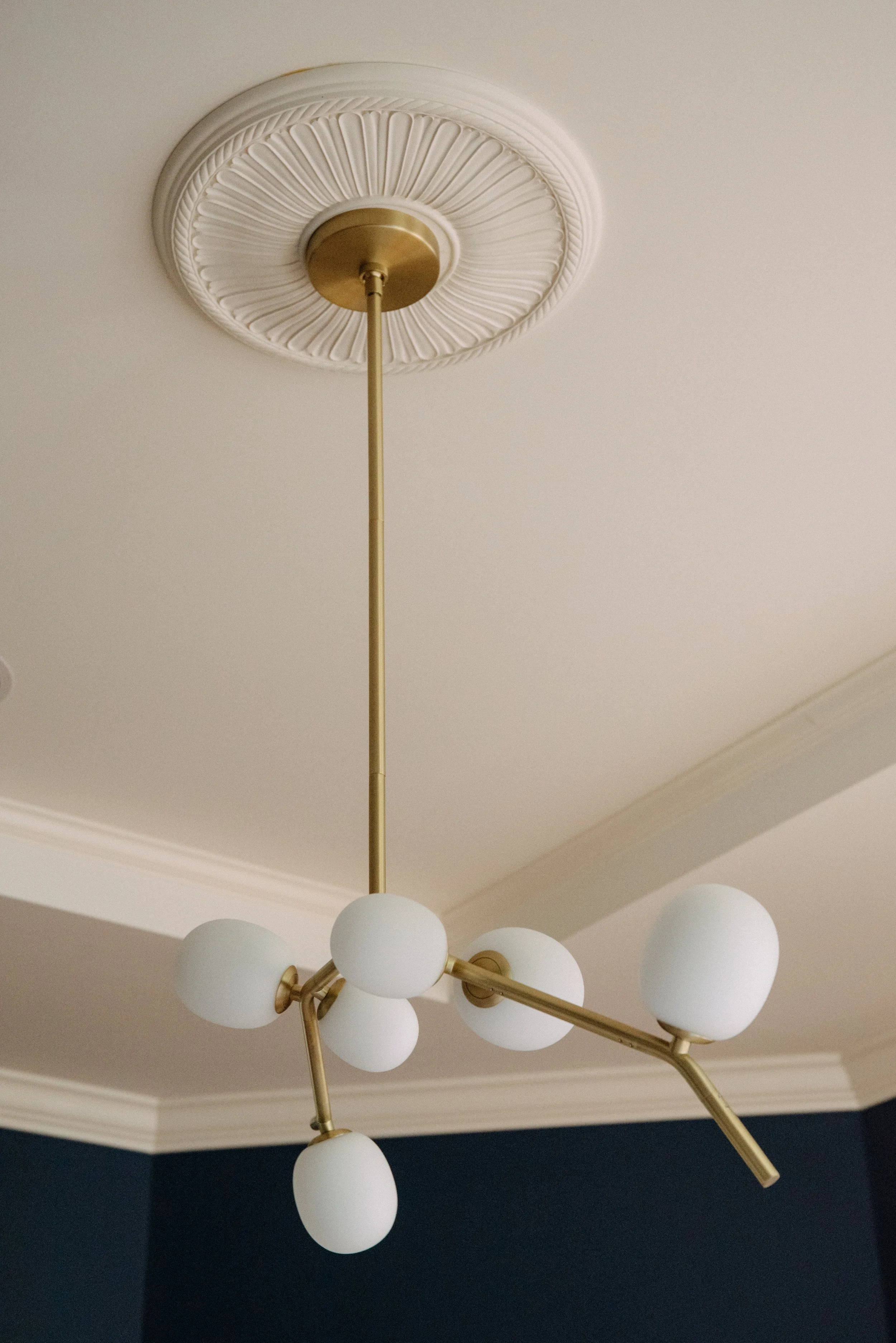 Modern chandelier with white globes and brass accents hanging from a ceiling medallion, over a room with dark walls.