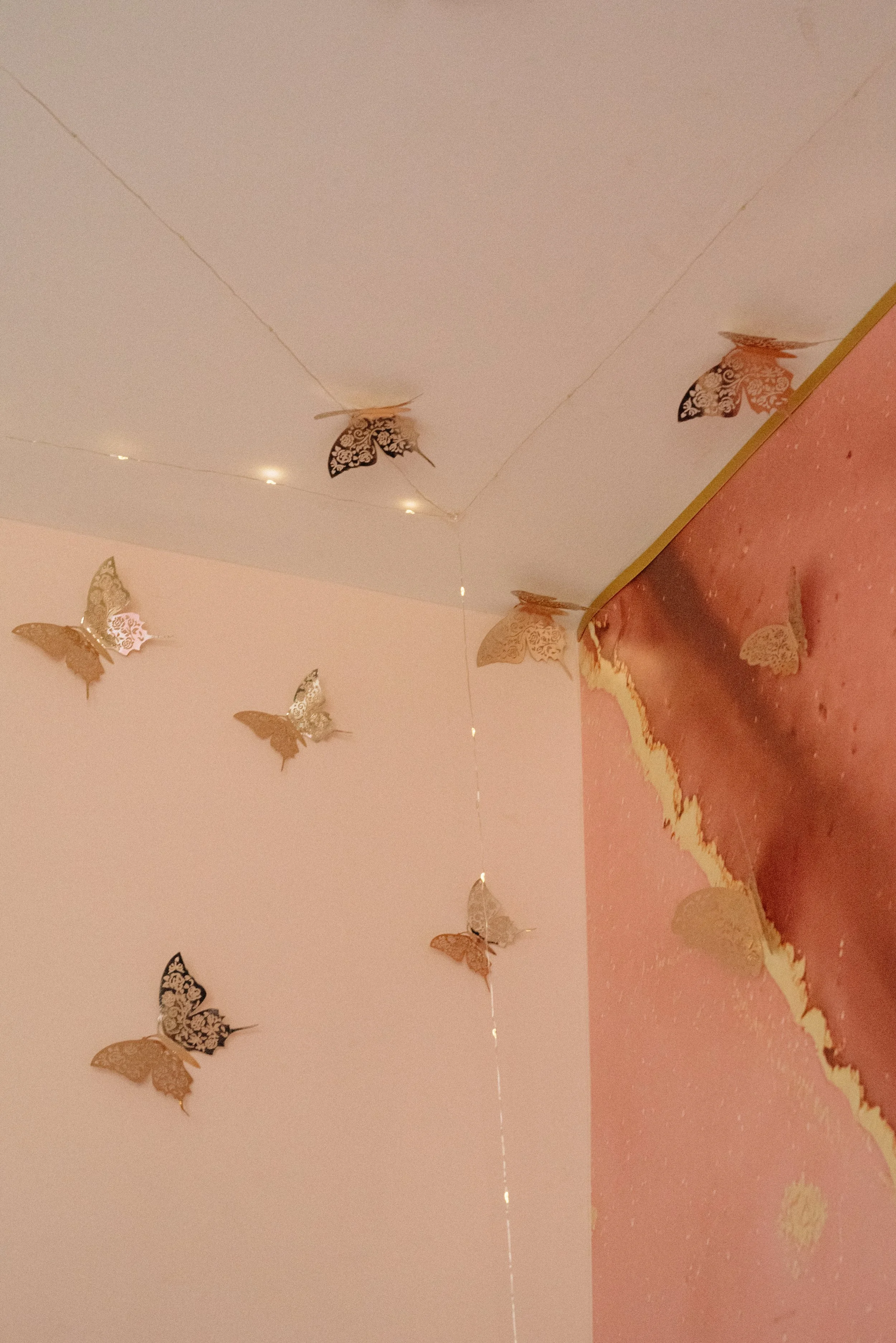 Decorative hanging butterflies with lace patterns on the ceiling near the corner meeting pink walls.