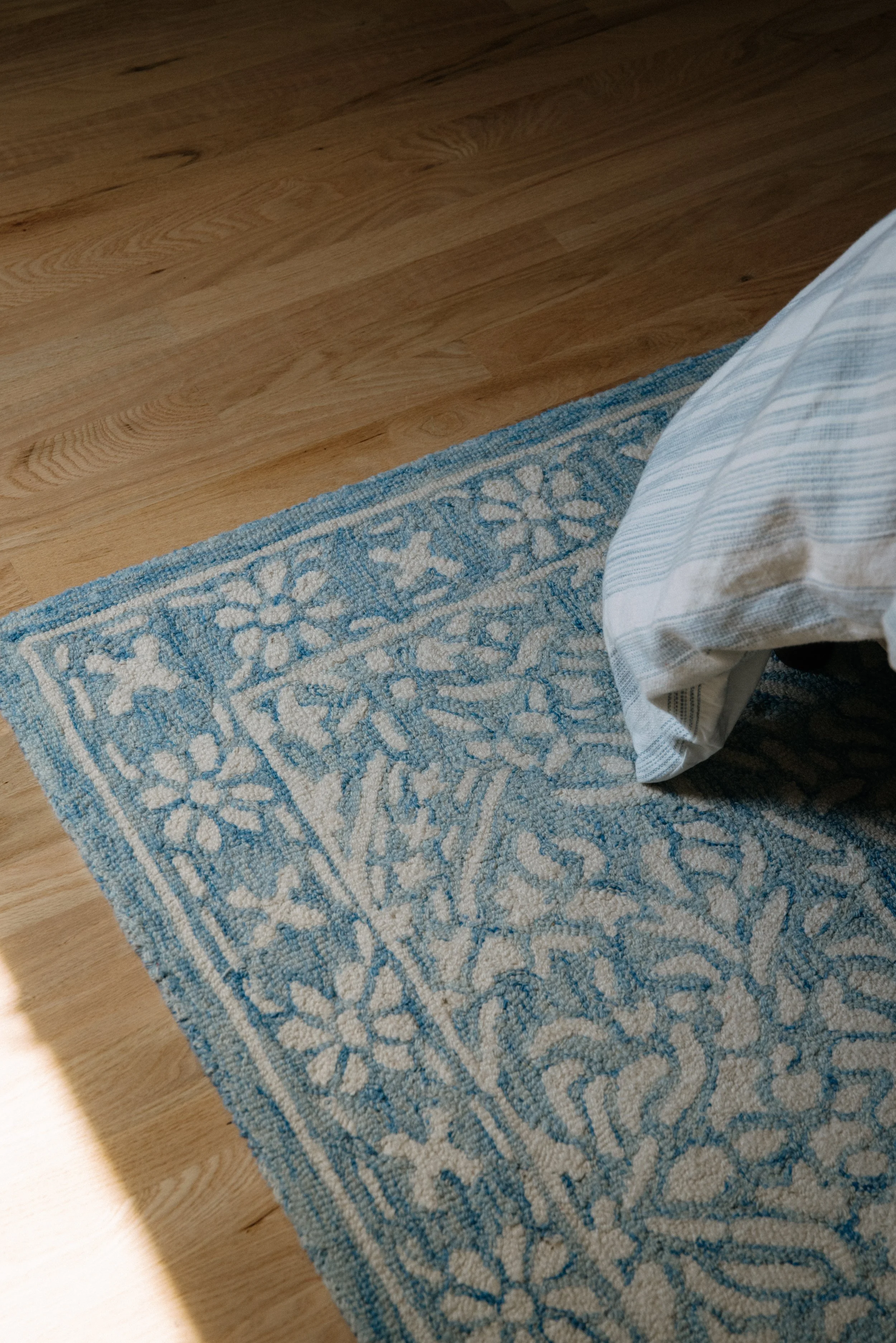 Close-up of a blue and white patterned rug on wooden floor with a pillow resting on it.