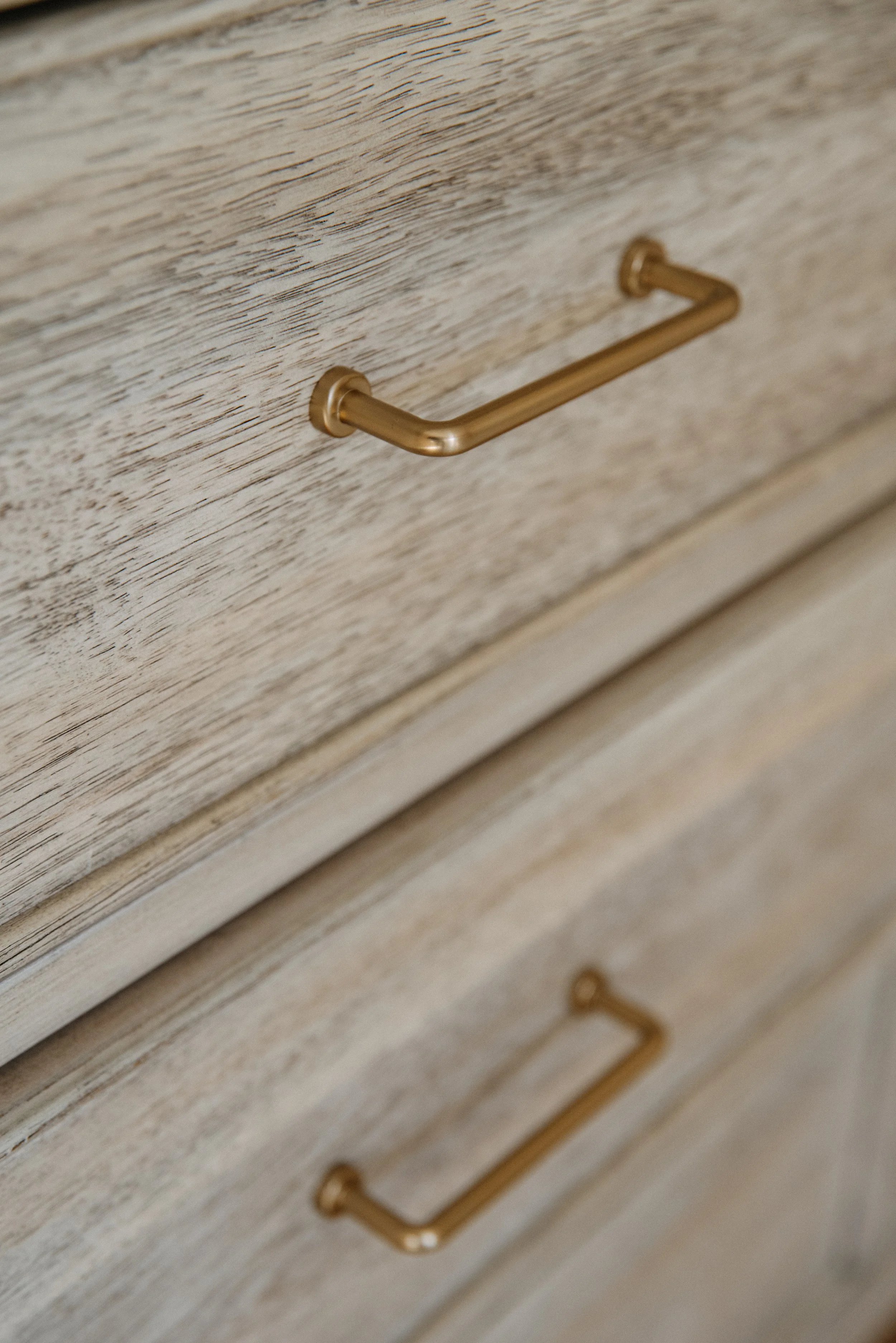 Close-up of a light wood drawer with gold-colored metal handles.